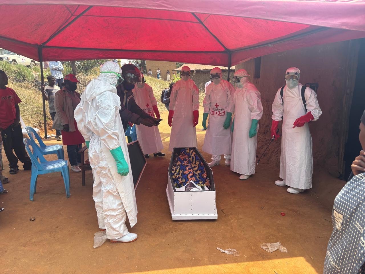 A Red Cross burial team in full protective gear prepares a coffin as relatives watch, part of a highly controlled process designed to prevent further Ebola transmission.