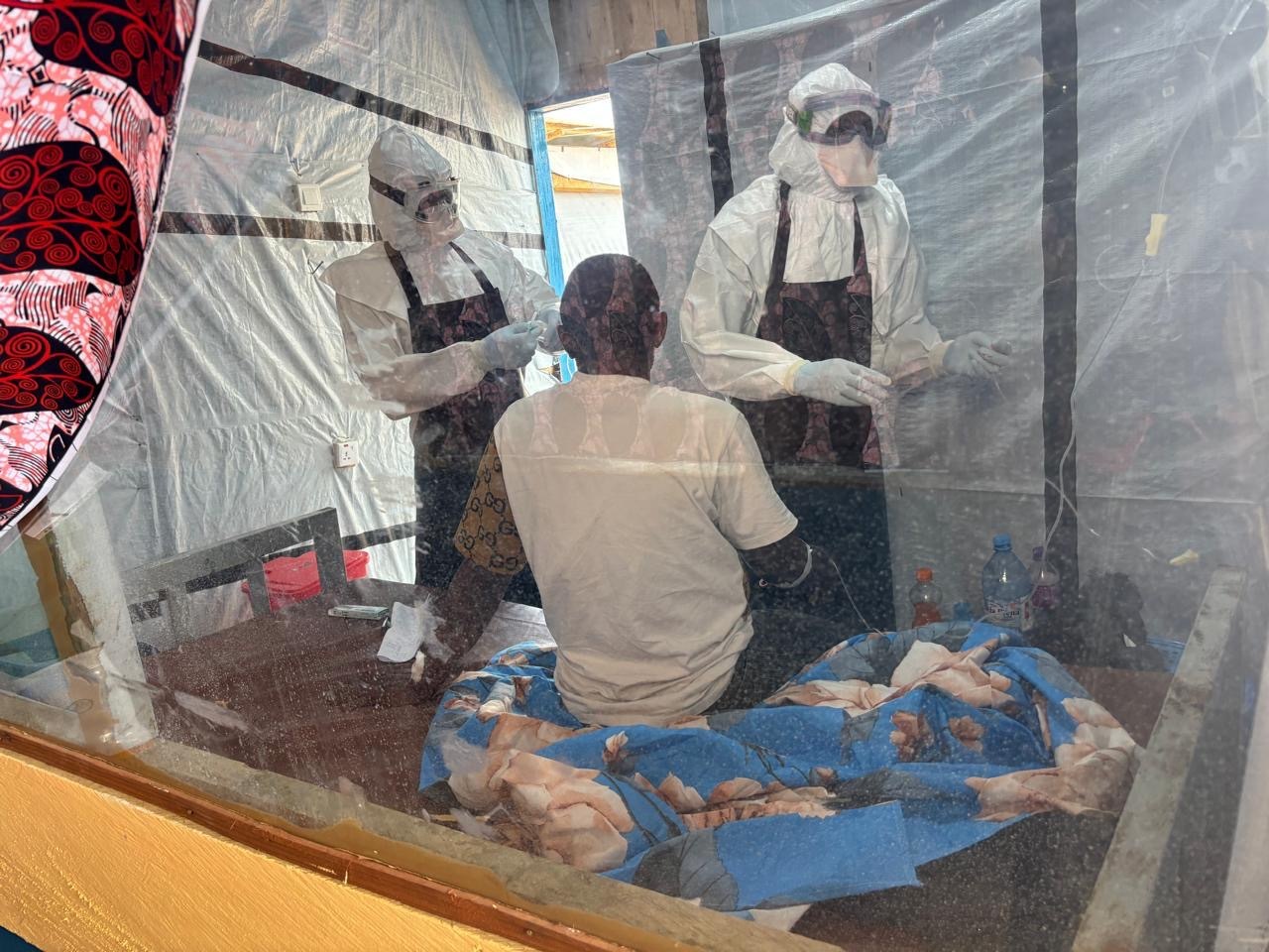 Health workers in protective suits attend to a patient in an isolation ward at the Rwampara treatment centre, where doctors say the Bundibugyo strain can move “silently” through the body until the final stages.
