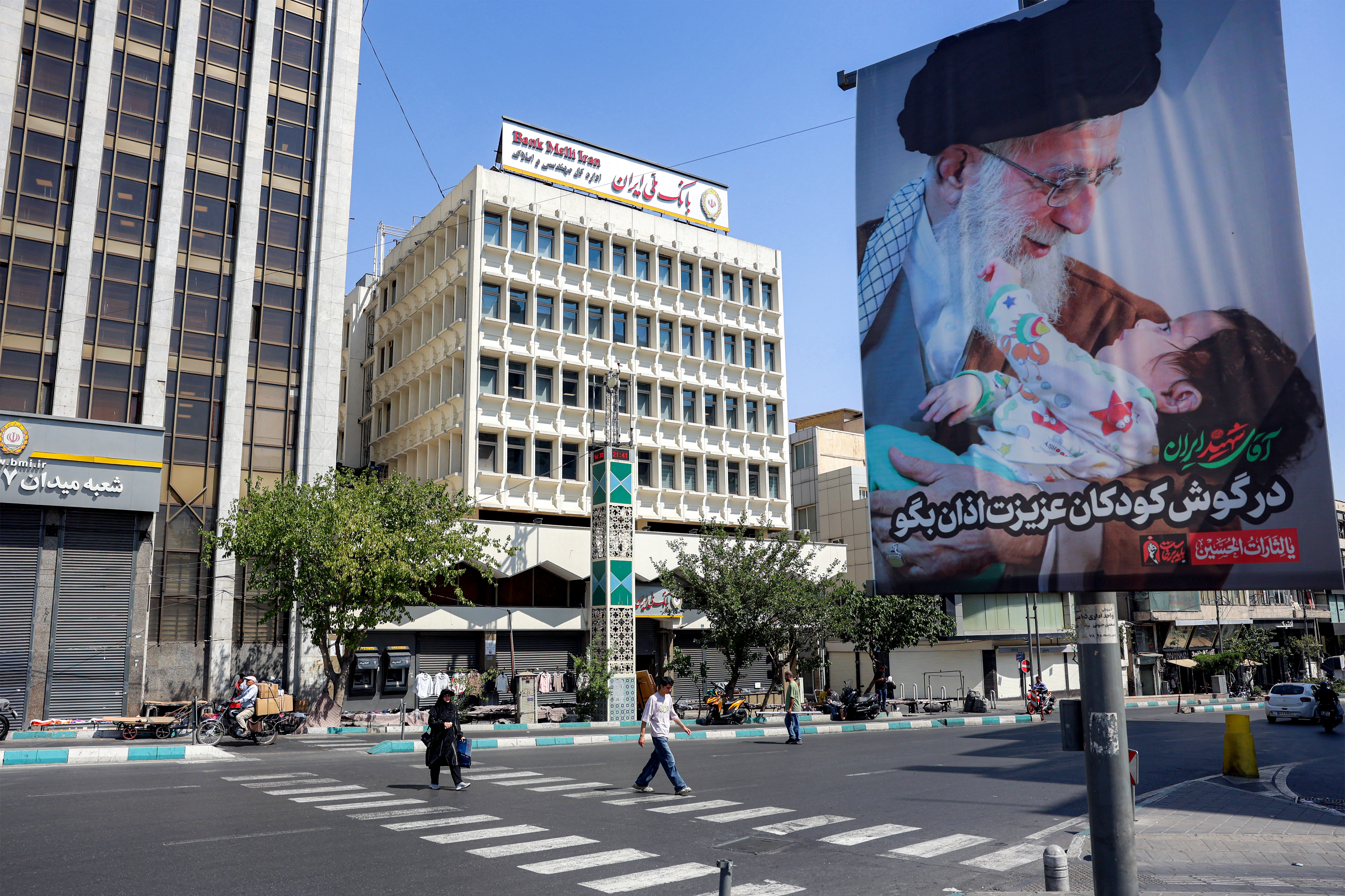 People cross a road past a mourning billboard depicting Iran's slain supreme leader Ali Khamenei, who was killed in a strike on the first day of the US-Israeli war against the Iran on February 28, in Tehran on June 30, 2026 ahead of his public funeral.