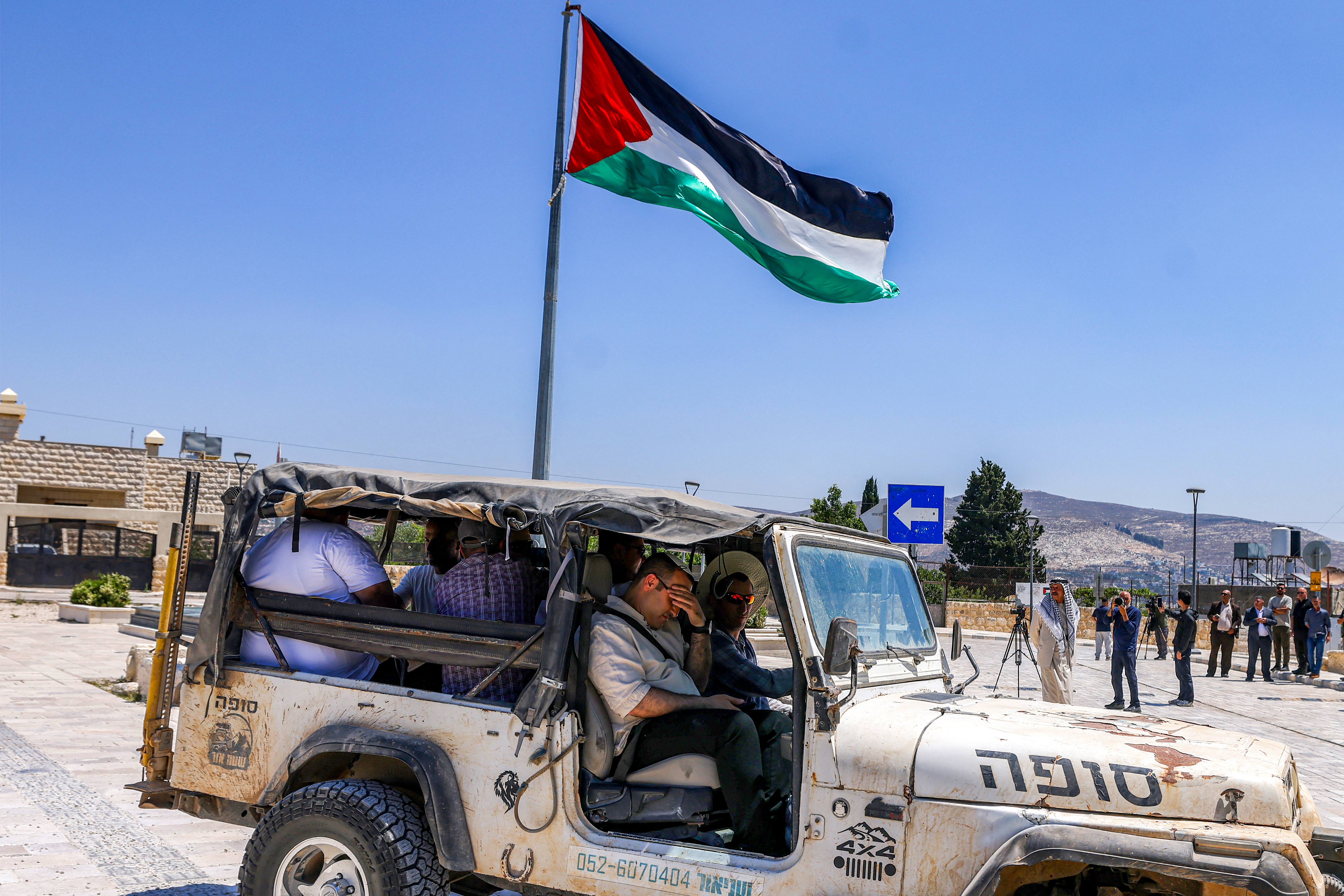 Israeli settlers sit in a four-wheel drive vehicle parked near a group of foreign diplomats accredited by the Palestinian Authority touring during an official visit at the archaeological site of Sebastia, north of Nablus in the occupied West Bank, on June 29, 2026.