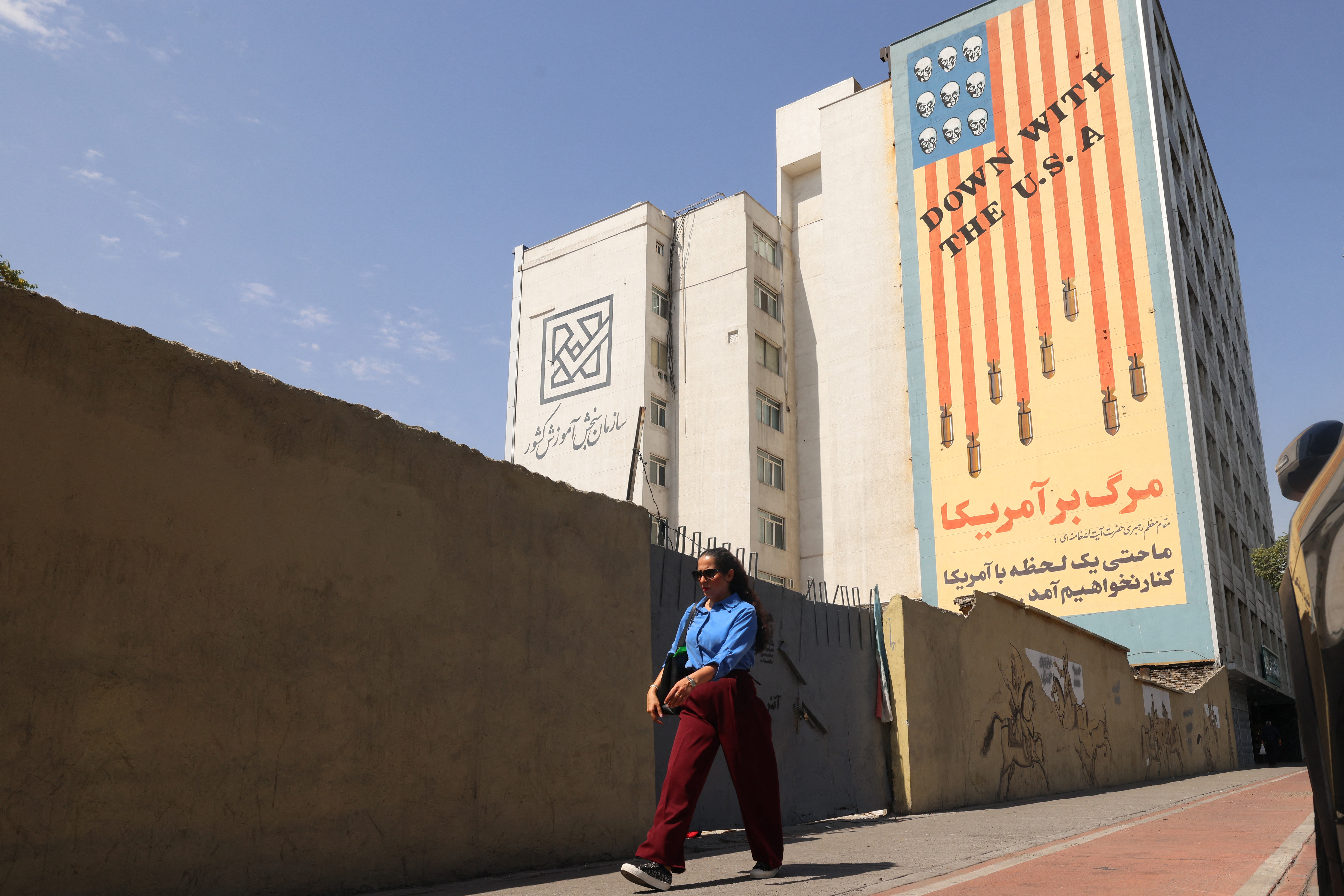 An Iranian woman walks past an anti-US banner in Tehran on July 19, 2026.