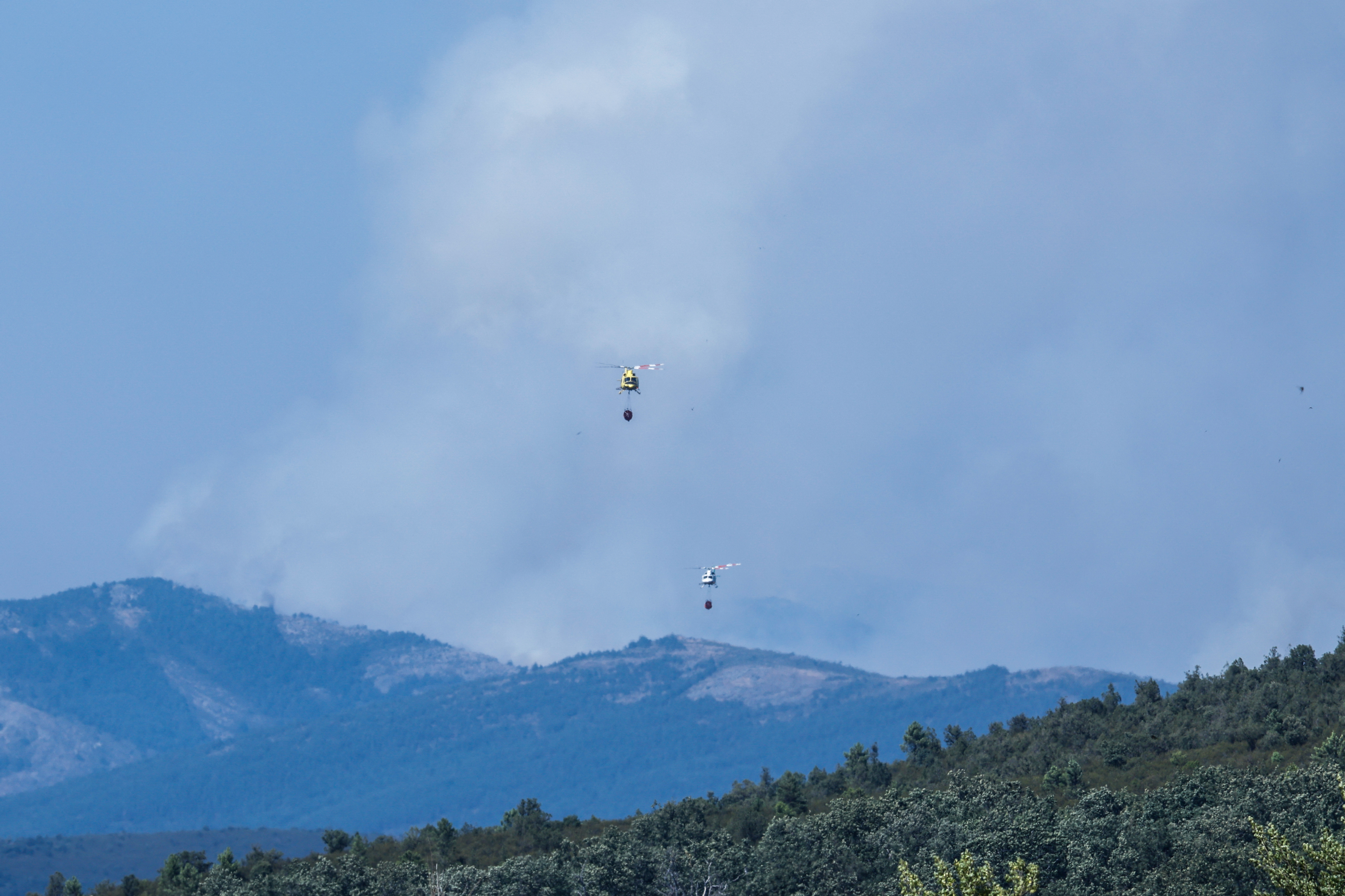 Smoke is seen as firefighter helicopters battle a huge wildfire north of Madrid that has devastated 29,000 hectares in the Guadalajar province, as seen from Tamajon, north of Madrid on July 21, 2026. (Photo by Pierre-Philippe MARCOU / AFP)
