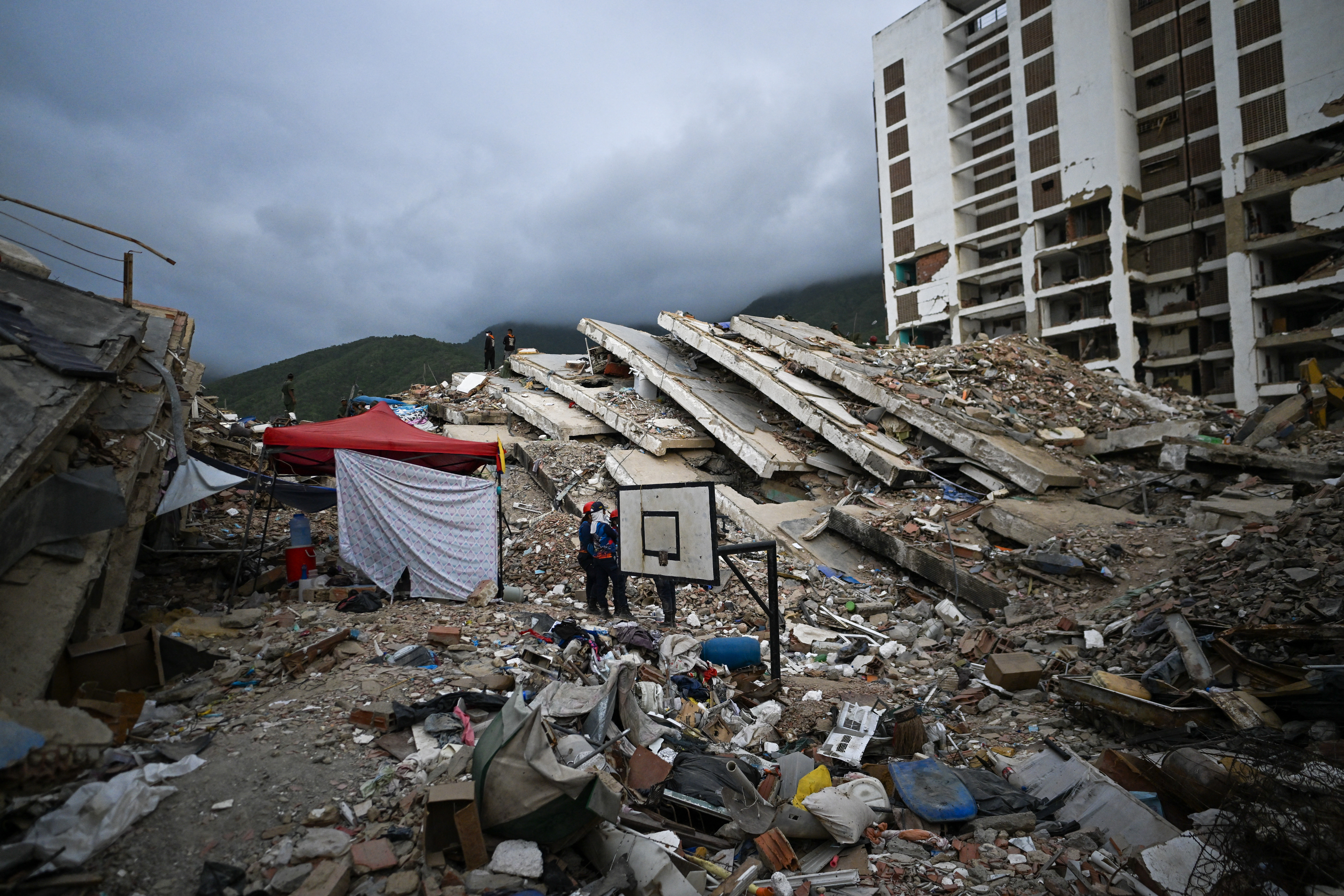 Volunteers talk as they take part in the search for bodies amid the rubble of an Obras del Poder Popular (OPP) building in Caraballeda, Venezuela, on July 22, 2026, nearly a month after the June 24 earthquakes.
