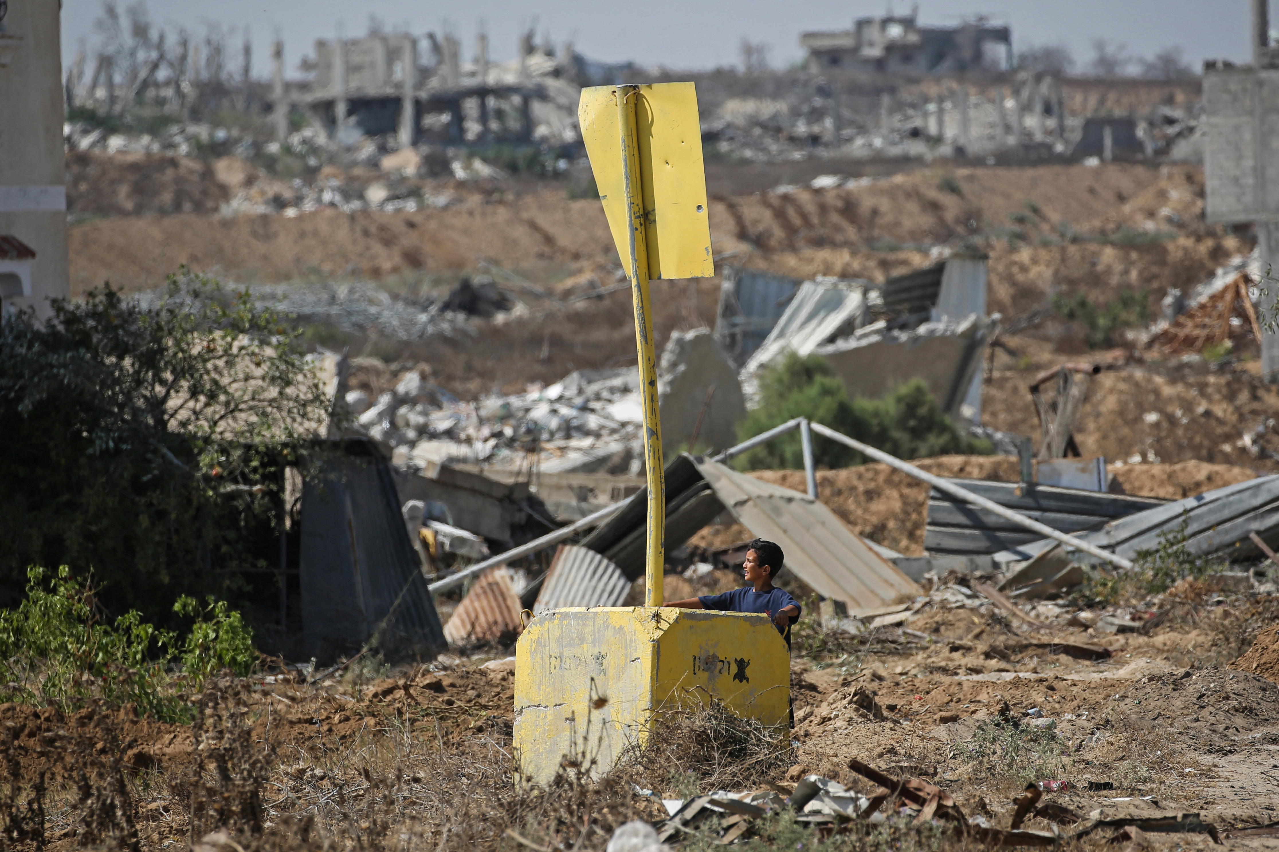 A Palestinian boy stands under a concrete block marking the 'Yellow Line' drawn by the Israeli military in the east of Deir al-Balah, central Gaza Strip on July 22, 2026, as violence has continued in Gaza despite the ceasefire.