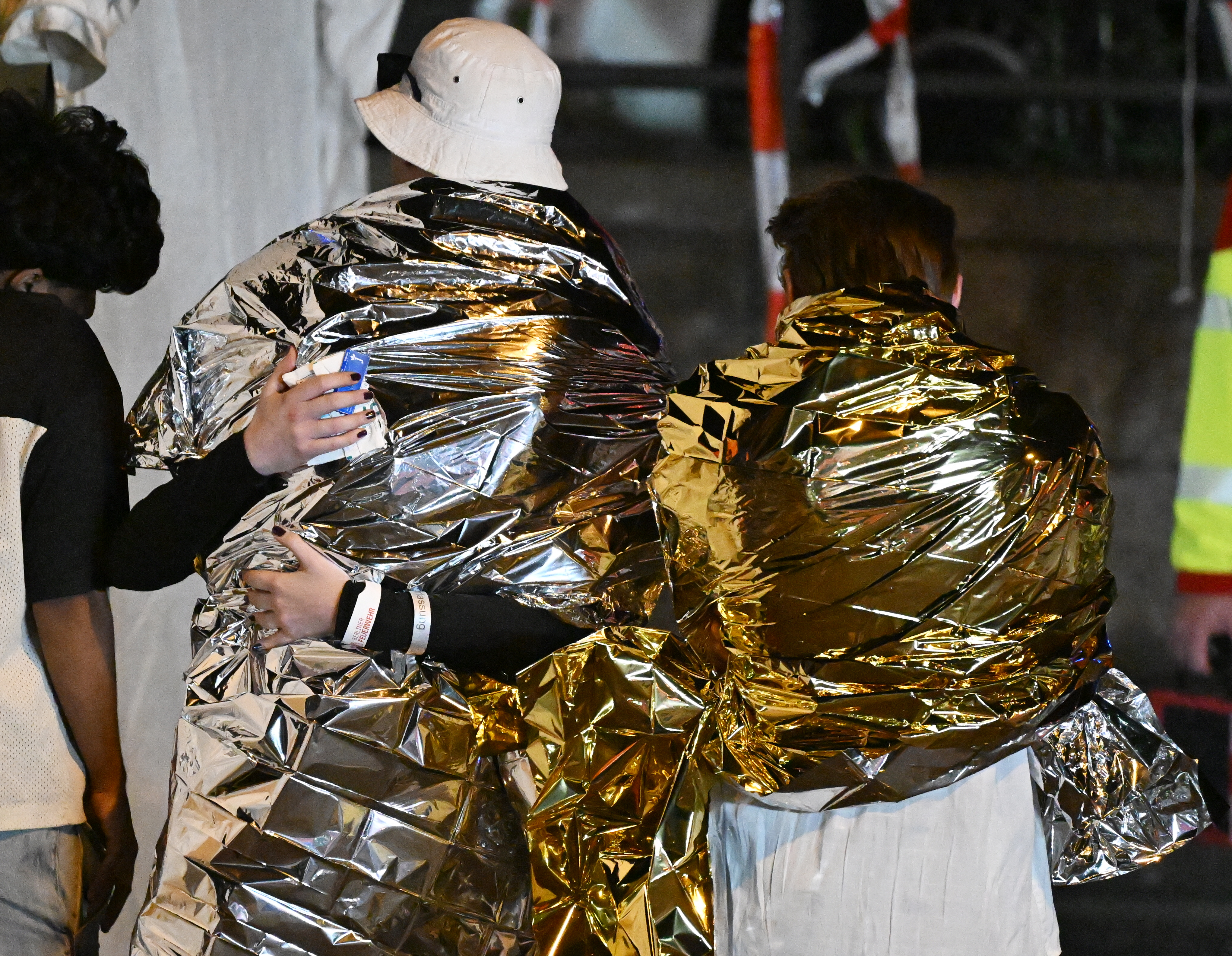 People wrapped in security blankets hug near the scene where one person was killed and around 15 injured after a car is believed to have hit the crowd on the outskirts of the Christopher Street Day (CSD) parade in Berlin, on July 25, 2026.