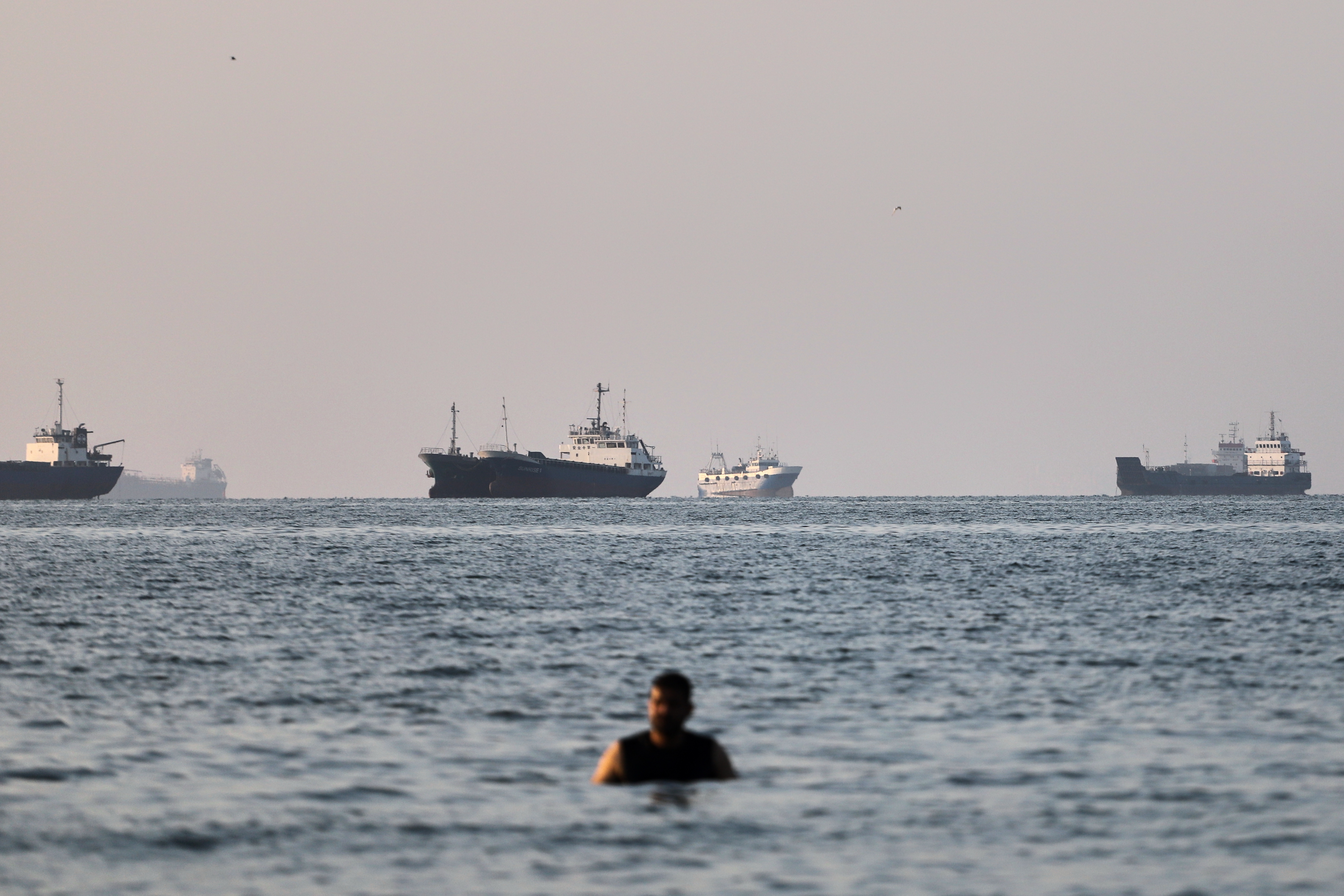 A person stands in shallow water as cargo and commercial vessels are anchored in the Strait of Hormuz off Bandar Abbas, Iran, on June 8, 2026 [Amirhosein Khorgooi/ISNA via AP]