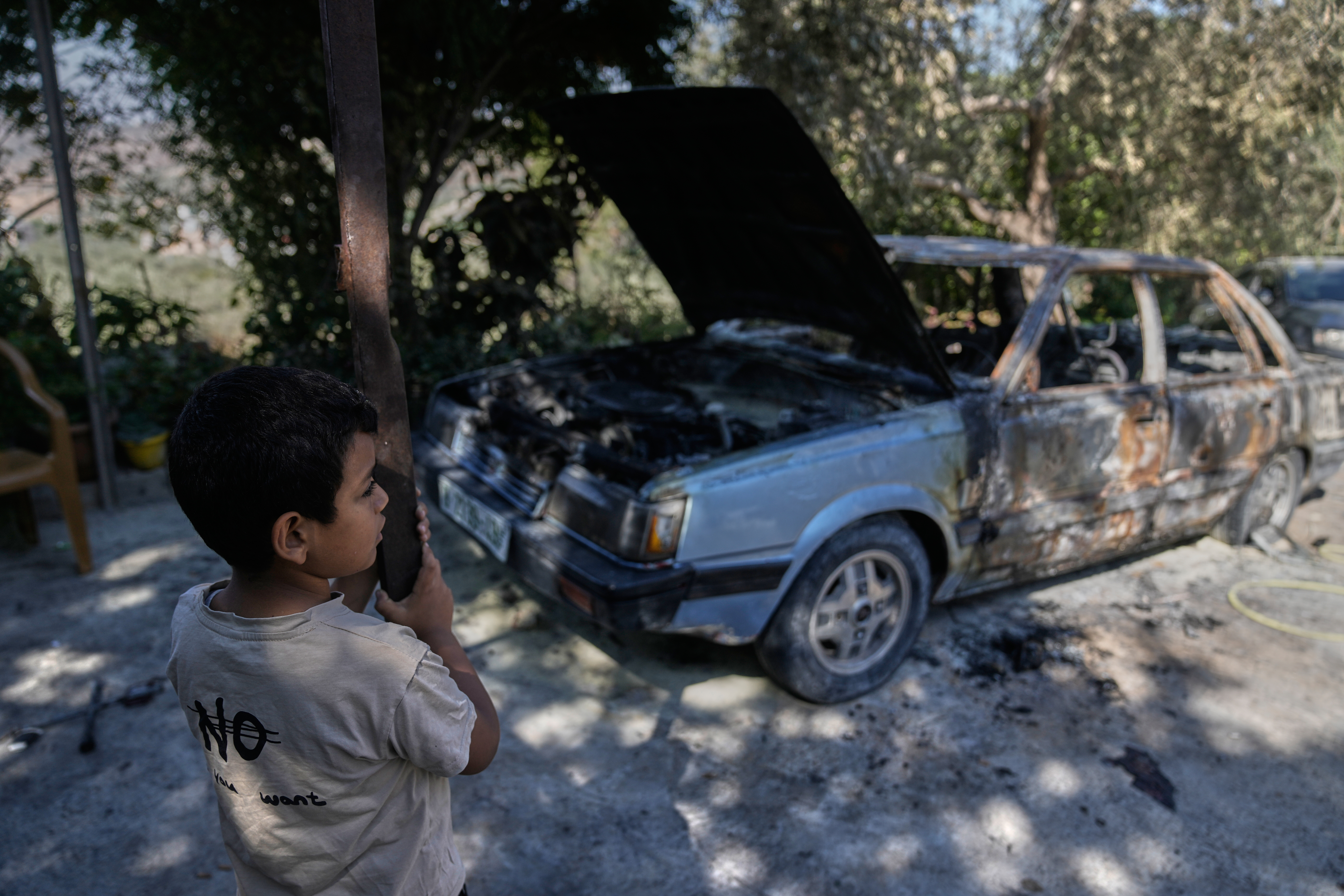 Palestinian child Yazan Hamad stands near his father's charred vehicle at the family house, following an Israeli settlers attack early morning, in the West Bank village of Ramin, east of Tulkarem Thursday, July 16, 2026. (AP Photo/Majdi Mohammed)