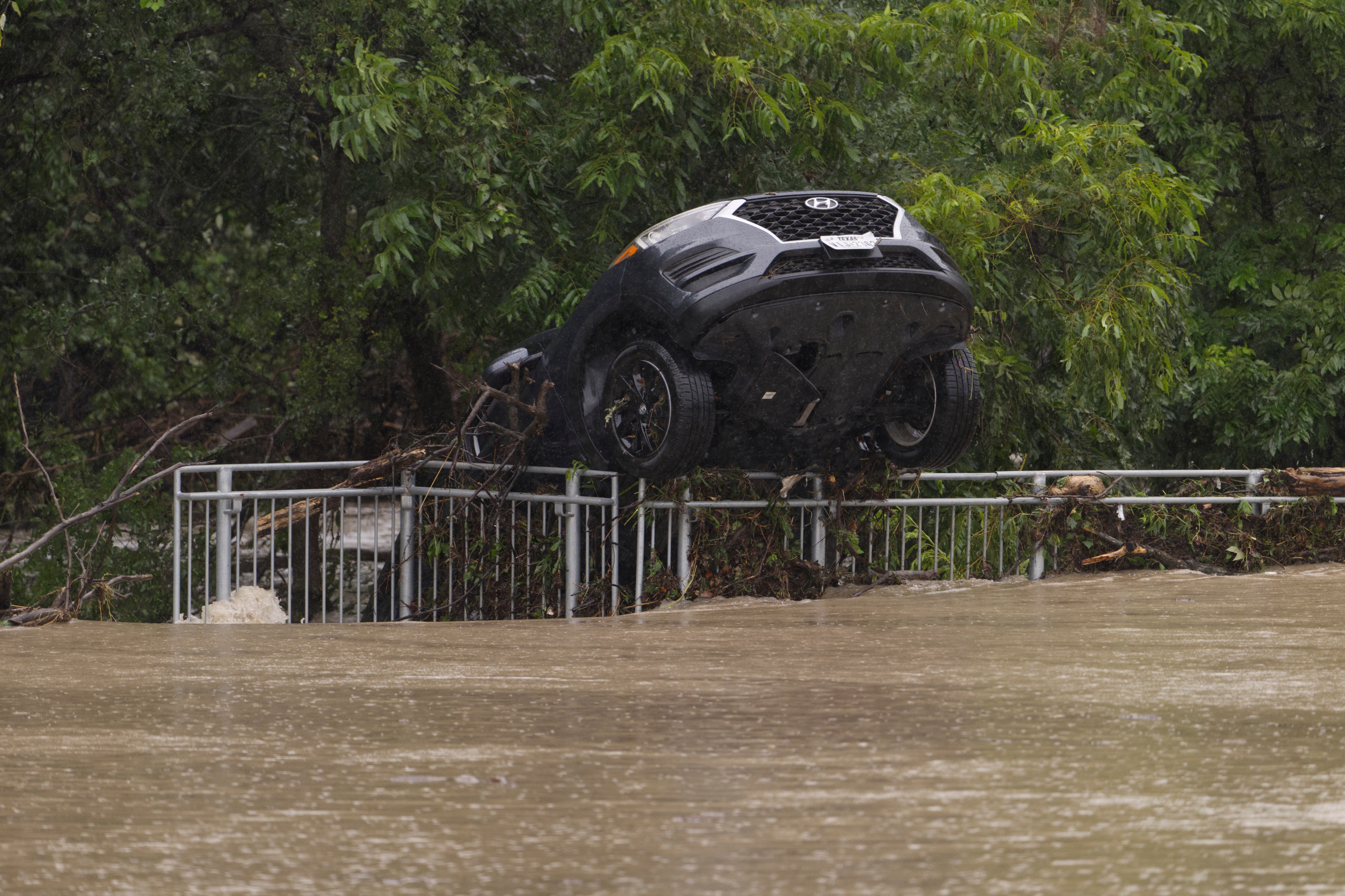 A flood-damaged car hangs from a fence on Wednesday, July 15, 2026, in Boerne, Texas. (AP Photo/Darren Abate)