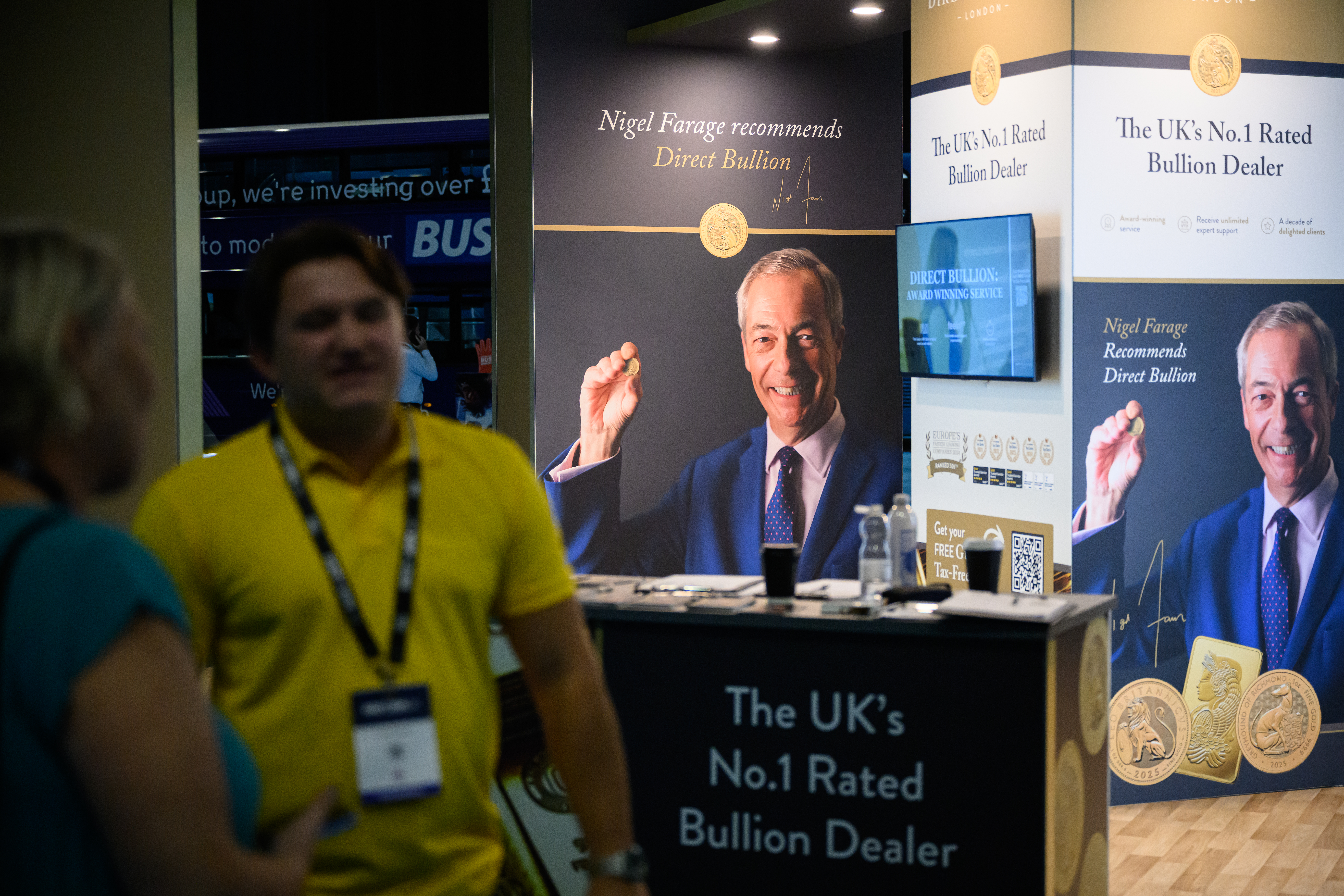 BIRMINGHAM, ENGLAND - SEPTEMBER 05: Reform UK Party Leader Nigel Farage appears on promotional posters for a gold bullion trading company in the main area of the party conference at National Exhibition Centre on September 05, 2025 in Birmingham, England. Members of Reform UK gather at the NEC Birmingham for the Party's two-day conference. (Photo by Leon Neal/Getty Images)