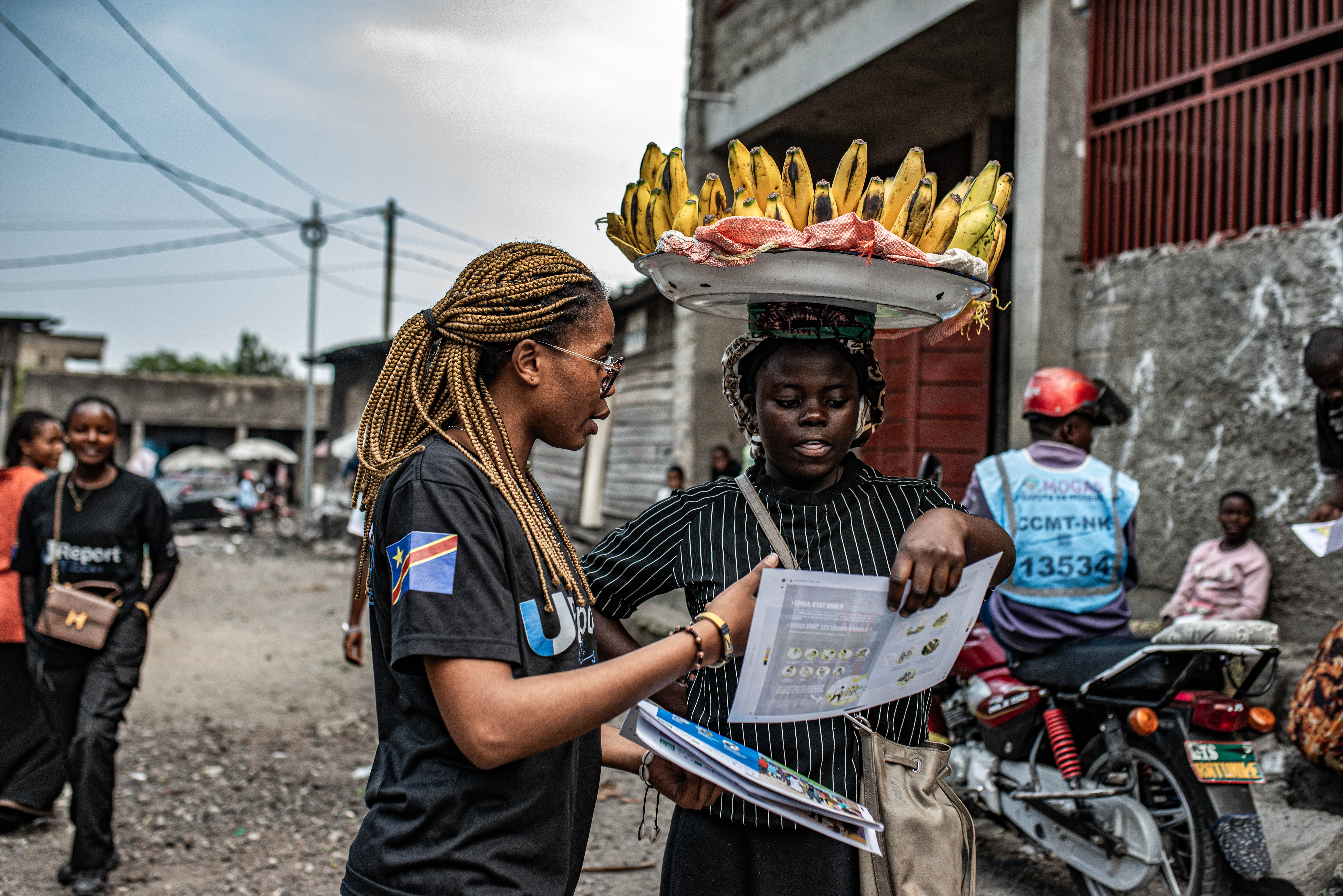 GOMA, DEMOCRATIC REPUBLIC OF CONGO - JUNE 24: A woman carrying plantains reads a pamphlet as workers with UNICEF's 'U-Report' group raise awareness about Ebola transmission at Alanine market on June 24, 2026 in Goma, Democratic Republic of Congo. On Monday, UN agencies announced that Ebola cases in the Democratic Republic of Congo had surpassed 1,000. Although testing capacity has recently improved, surveillance and contact tracing remain constrained by insecurity and restricted access in Ituri province, the heart of the current outbreak, north of Goma. (Photo by Daniel Buuma/Getty Images)