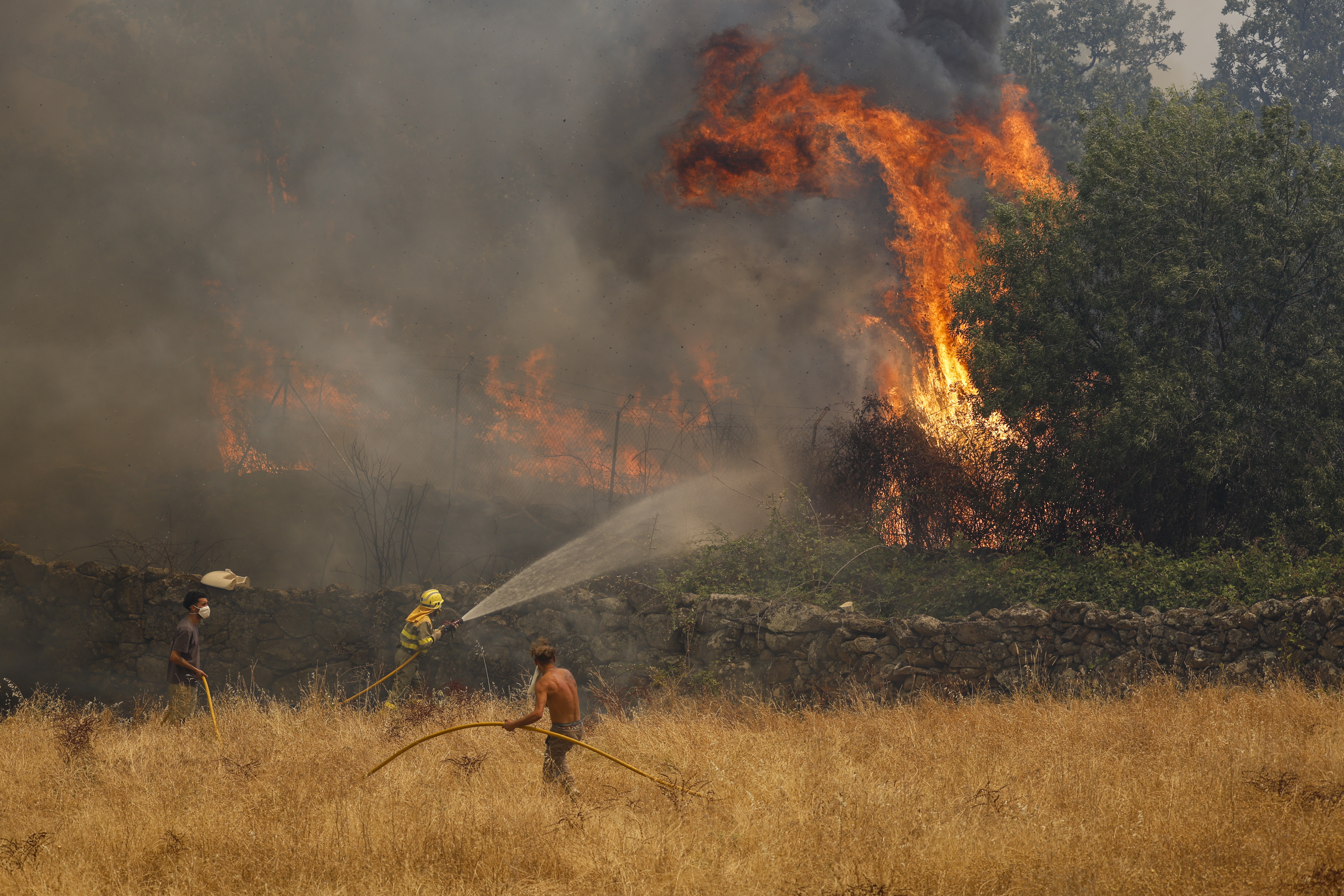 Firefighters and civillians attempt to extinguish a wildfire as it approaches houses on July 24, 2026 in El Tiemblo, in Ávila province, Spain. The Spanish interior minister declared a state of emergency as more than 11,500 people were forced to evacuate their homes to wildfires across the country. (Photo by Pablo Blazquez Dominguez/Getty)