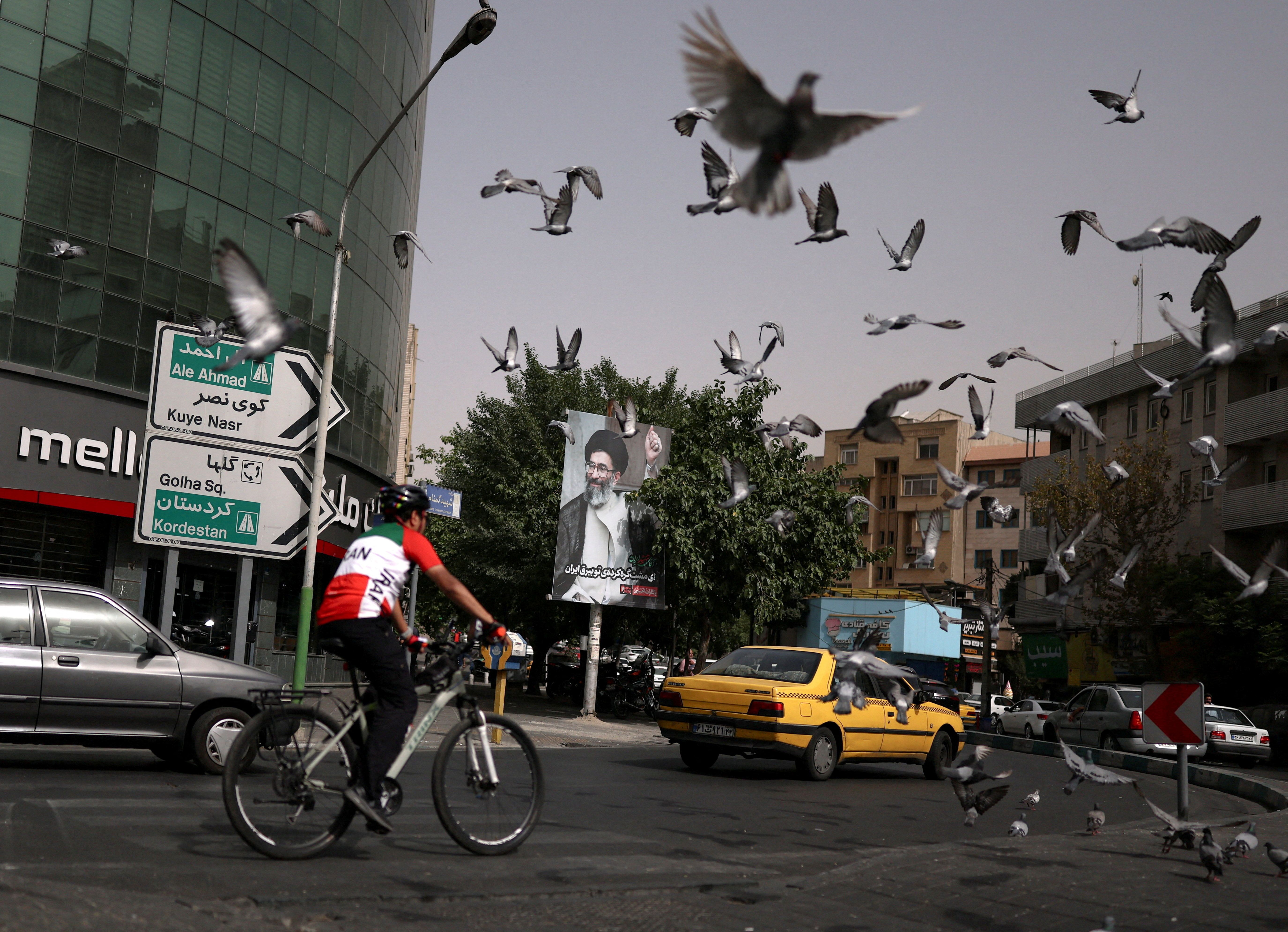 A man rides a bicycle as birds fly near a banner featuring an earlier image of Iran's late Supreme Leader Ayatollah Ali Khamenei on a street in Tehran, Iran, July 2, 2026. REUTERS/Mohammed Salem Foreign media in Iran operate under guidelines set by the Ministry of Culture and Islamic Guidance, which regulates press activity and permissions ISRAEL OUT. NO COMMERCIAL OR EDITORIAL SALES IN ISRAEL. NO ACCESS FOR ISRAELI MEDIA. NO USE BBC PERSIAN. NO USE VOA PERSIAN. NO USE MANOTO. NO USE IRAN INTERNATIONAL. NO USE RADIO FARDA. DIGITAL: NO USE BBC PERSIAN. NO USE VOA PERSIAN. NO USE MANOTO. NO USE IRAN INTERNATIONAL. NO USE RADIO FARDA. TPX IMAGES OF THE DAY