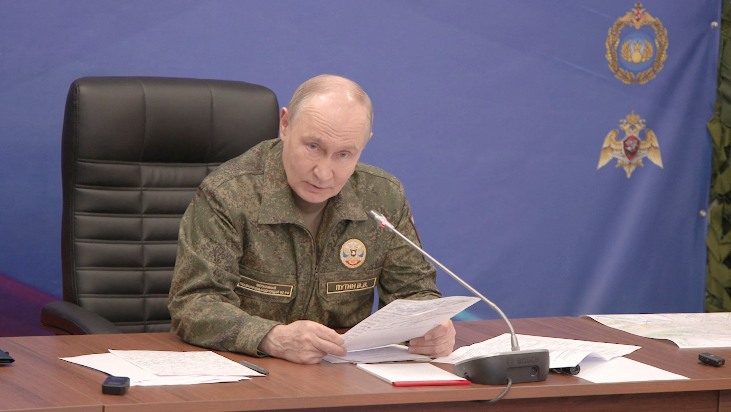 Russian President Vladimir Putin holds papers as he speaks at a desk.