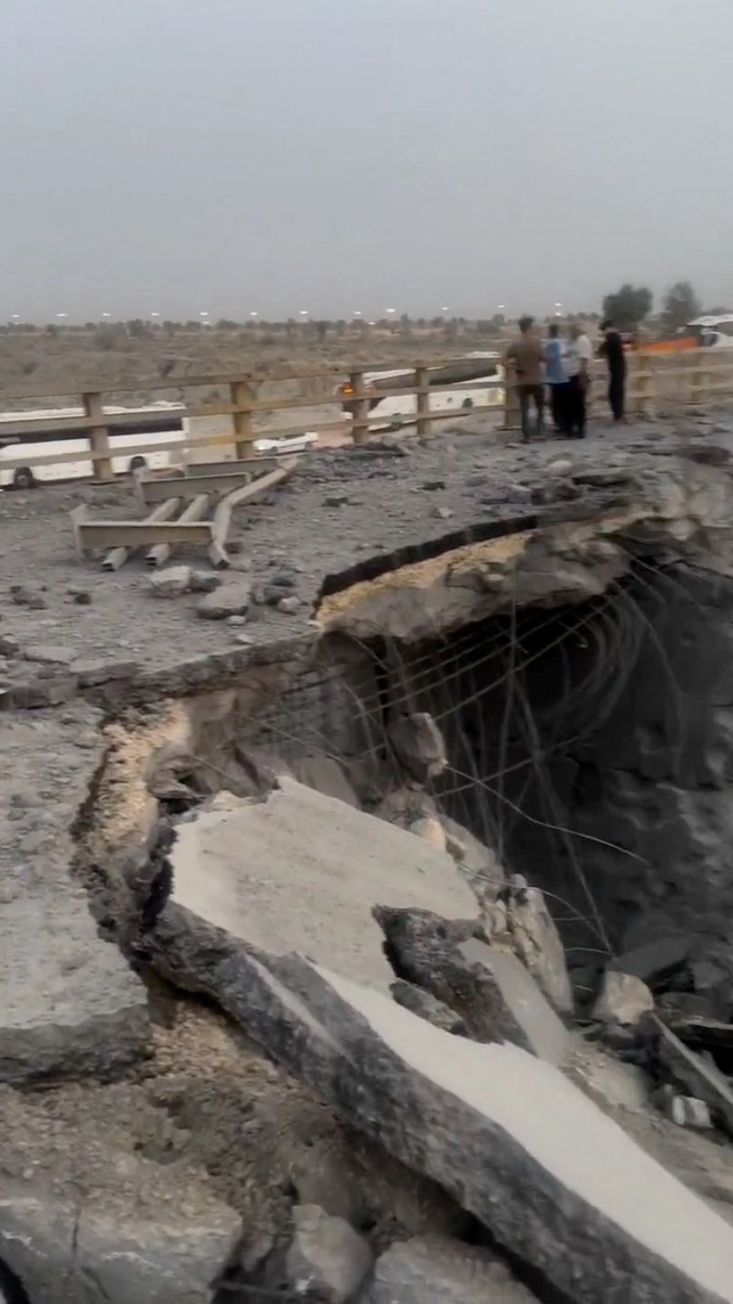 People stand near a damaged part of a bridge.