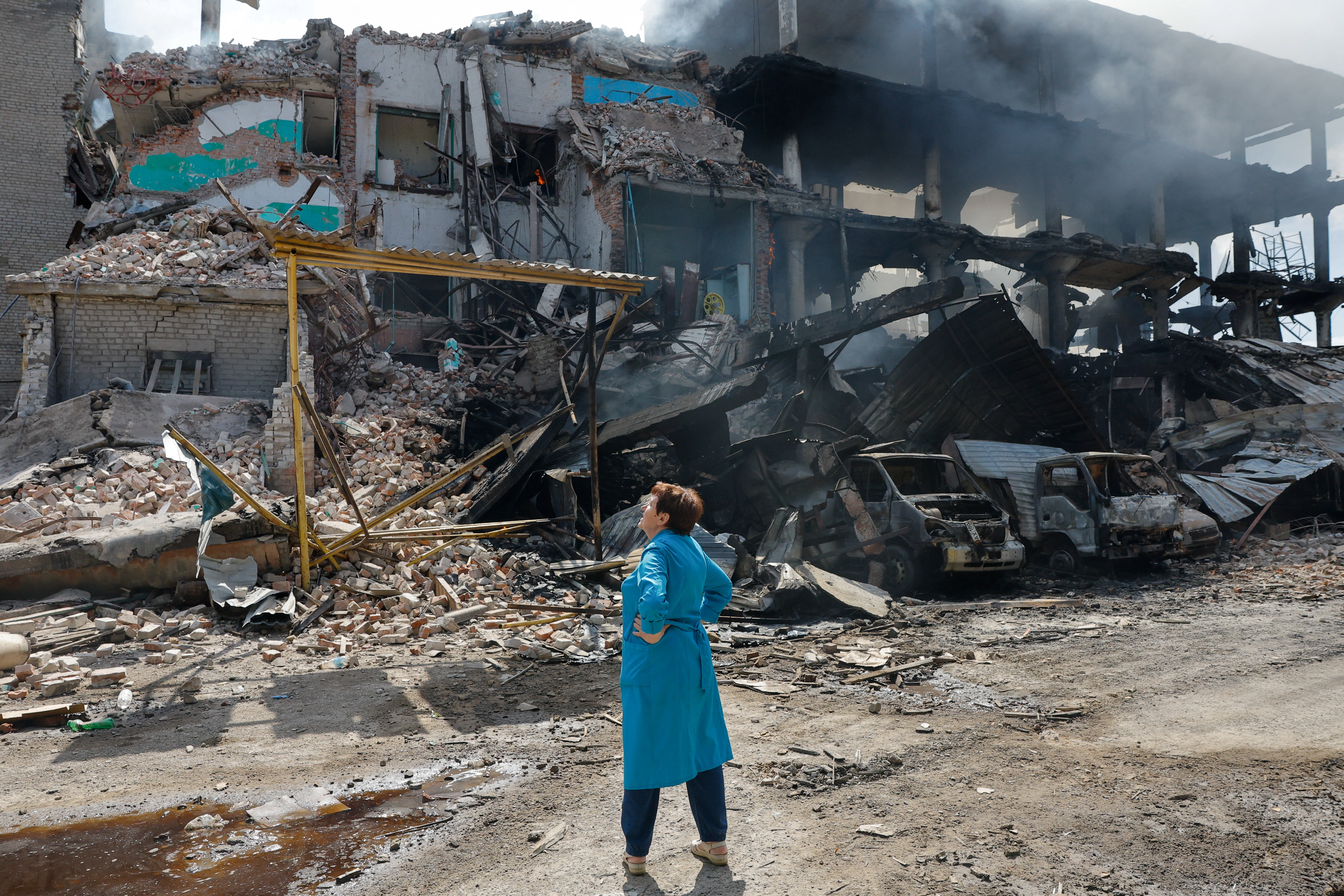 A woman stands in front of a destroyed building.