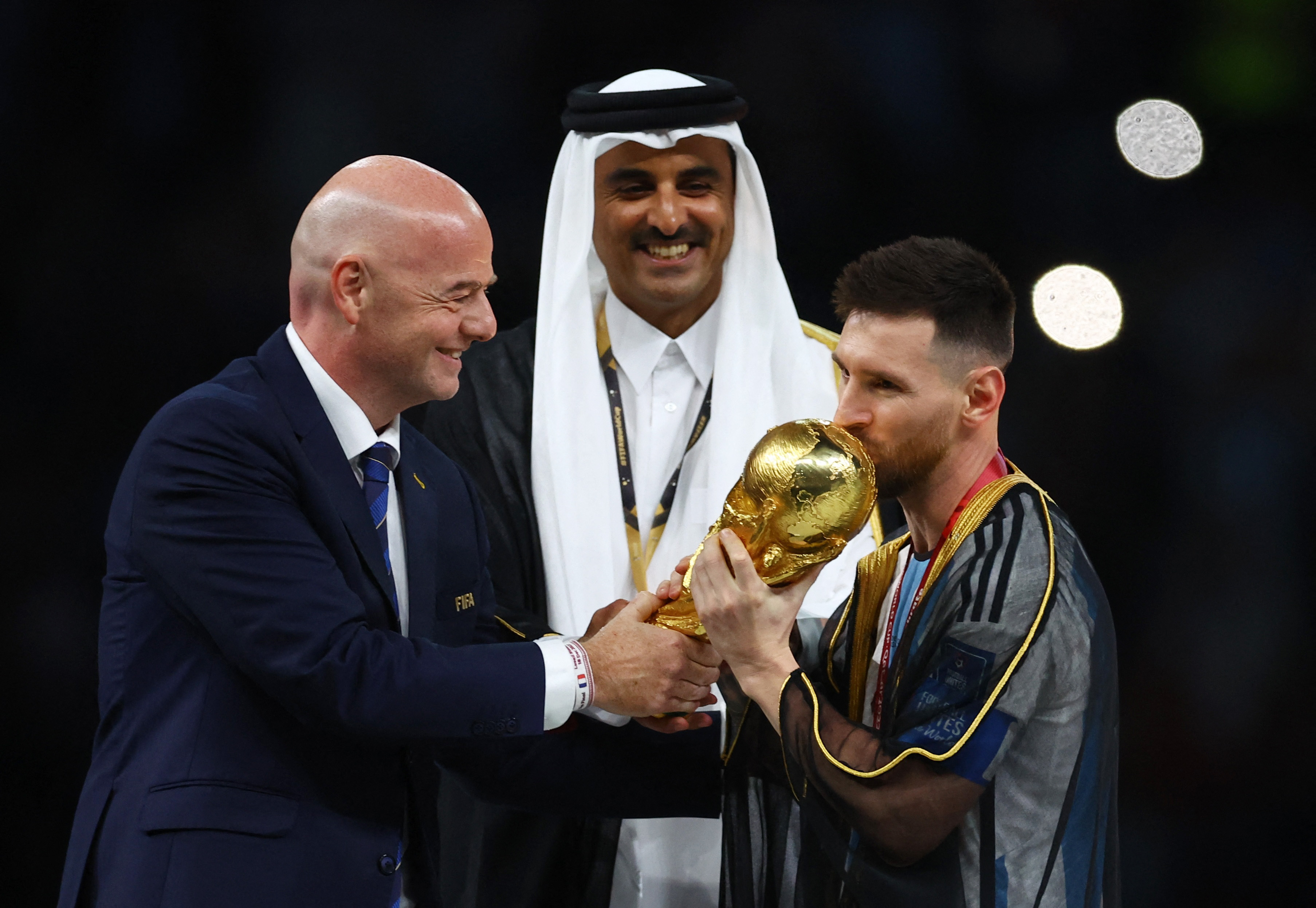 Soccer Football - FIFA World Cup Qatar 2022 - Final - Argentina v France - Lusail Stadium, Lusail, Qatar - December 18, 2022 Argentina's Lionel Messi kisses the trophy as he is presented it by FIFA president Gianni Infantino alongside Emir of Qatar Sheikh Tamim bin Hamad Al Thani REUTERS/Kai Pfaffenbach