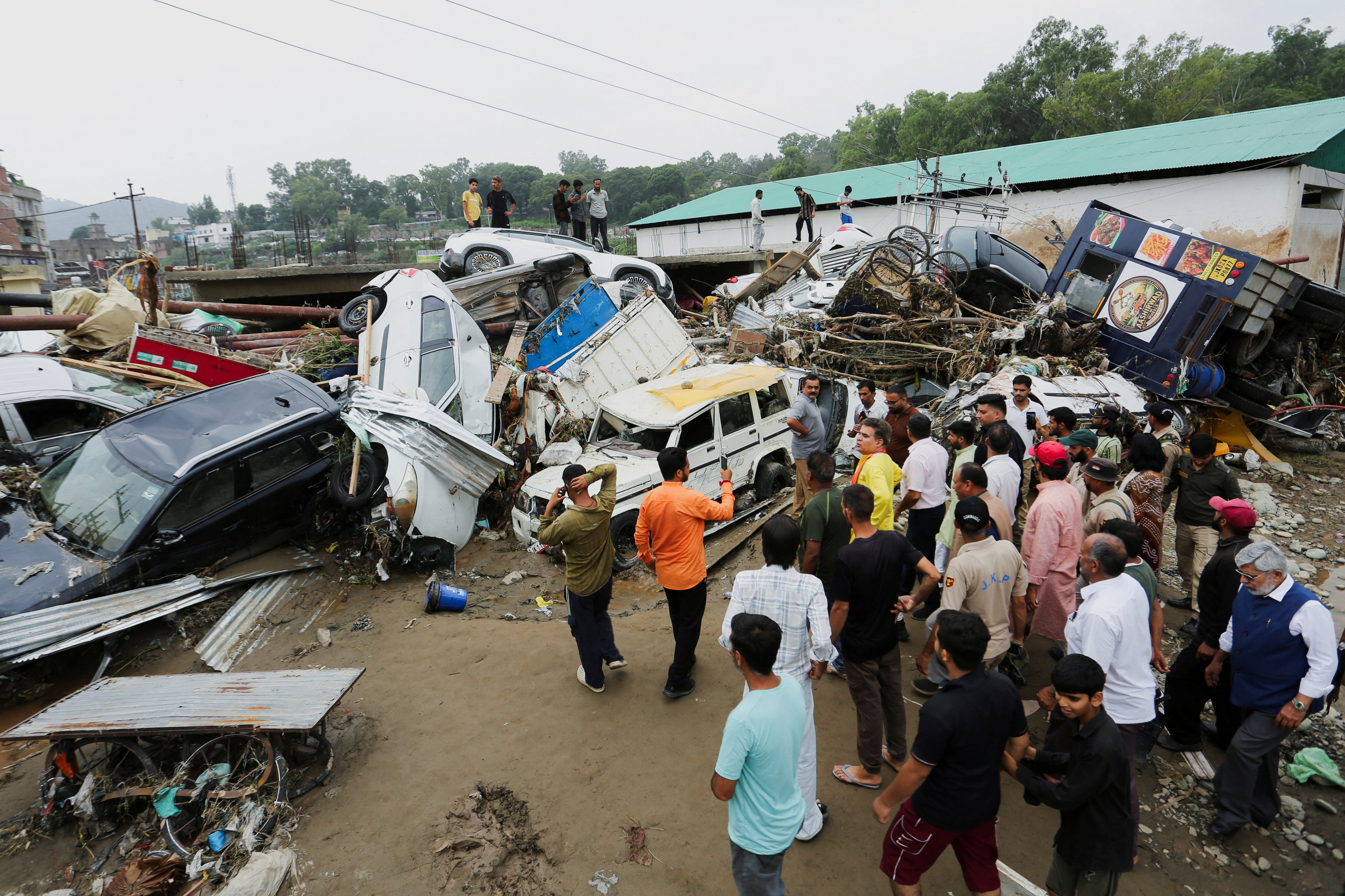 People gather next to vehicles piled up after a flash flood in Rajouri, Indian Kashmir, July 19, 2026. REUTERS/Stringer