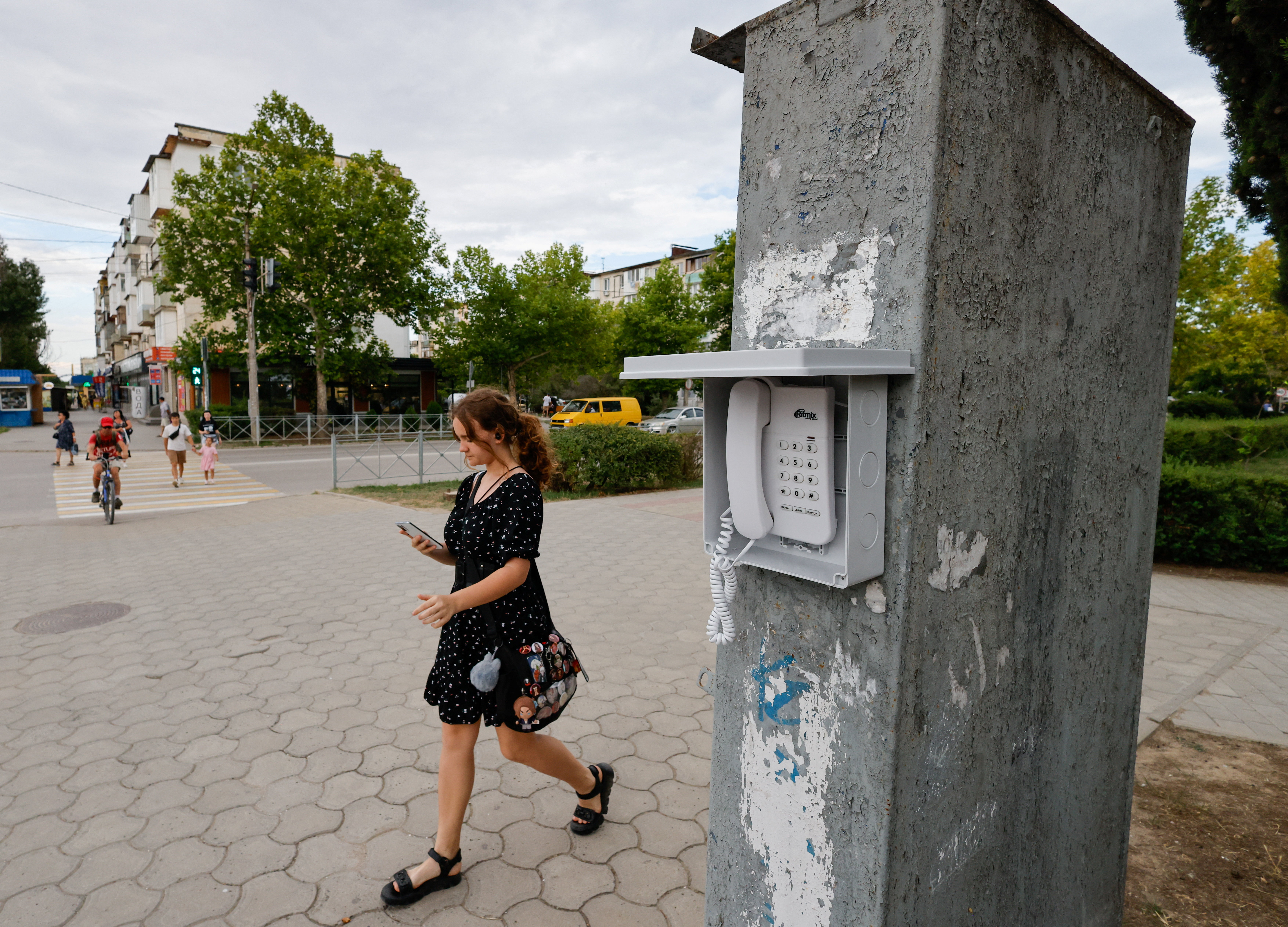 A woman uses a mobile phone as she walks past a landline public street phone for communication with emergency services when there are disruptions to the mobile network, amid the Russia-Ukraine conflict, in the Black Sea resort city of Yevpatoriya, Crimea, July 21, 2026. REUTERS/Alexey Pavlishak