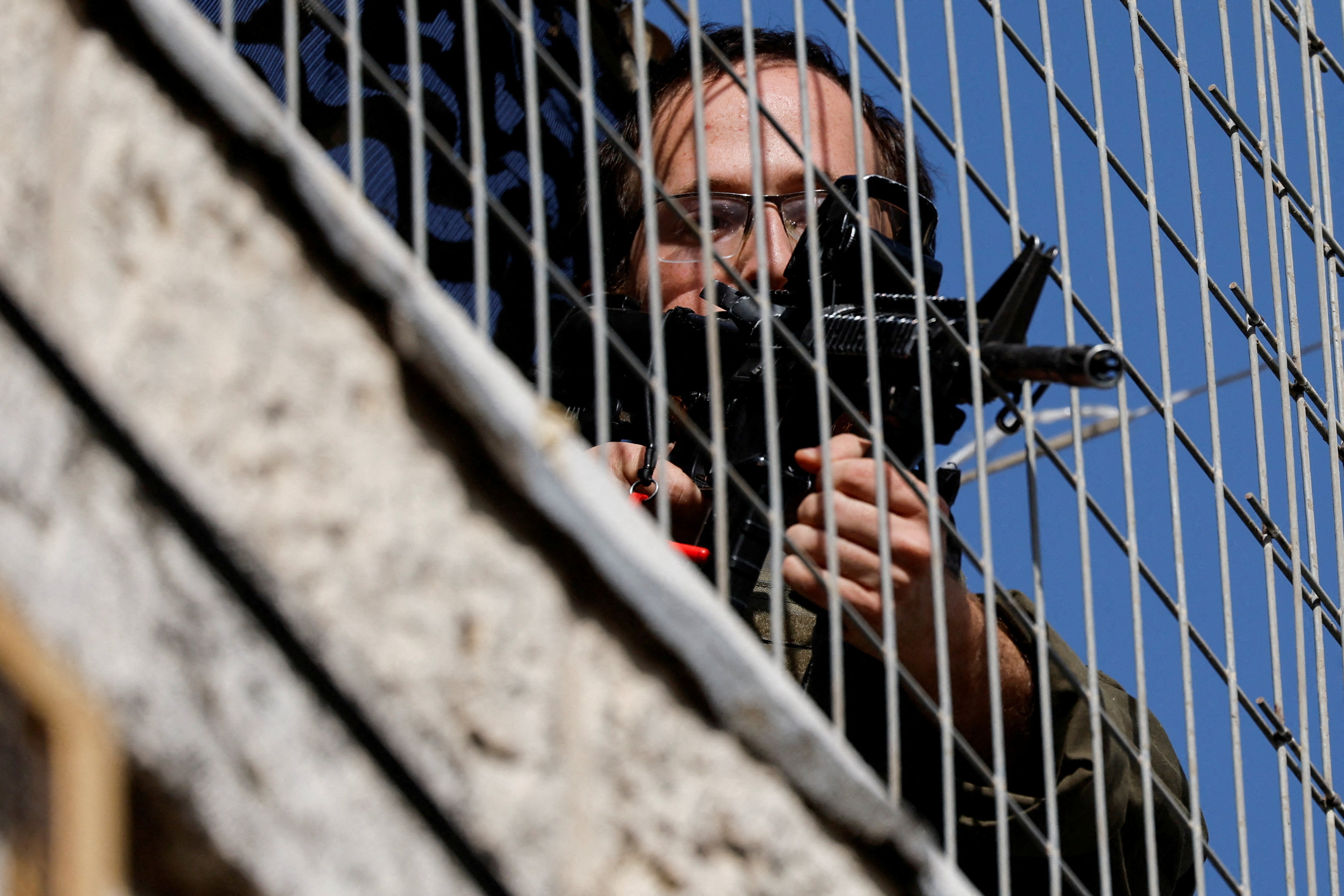 An Israeli soldier aims his weapon through a metal fence, in the Israeli-occupied West Bank, July 25, 2026. [REUTERS]