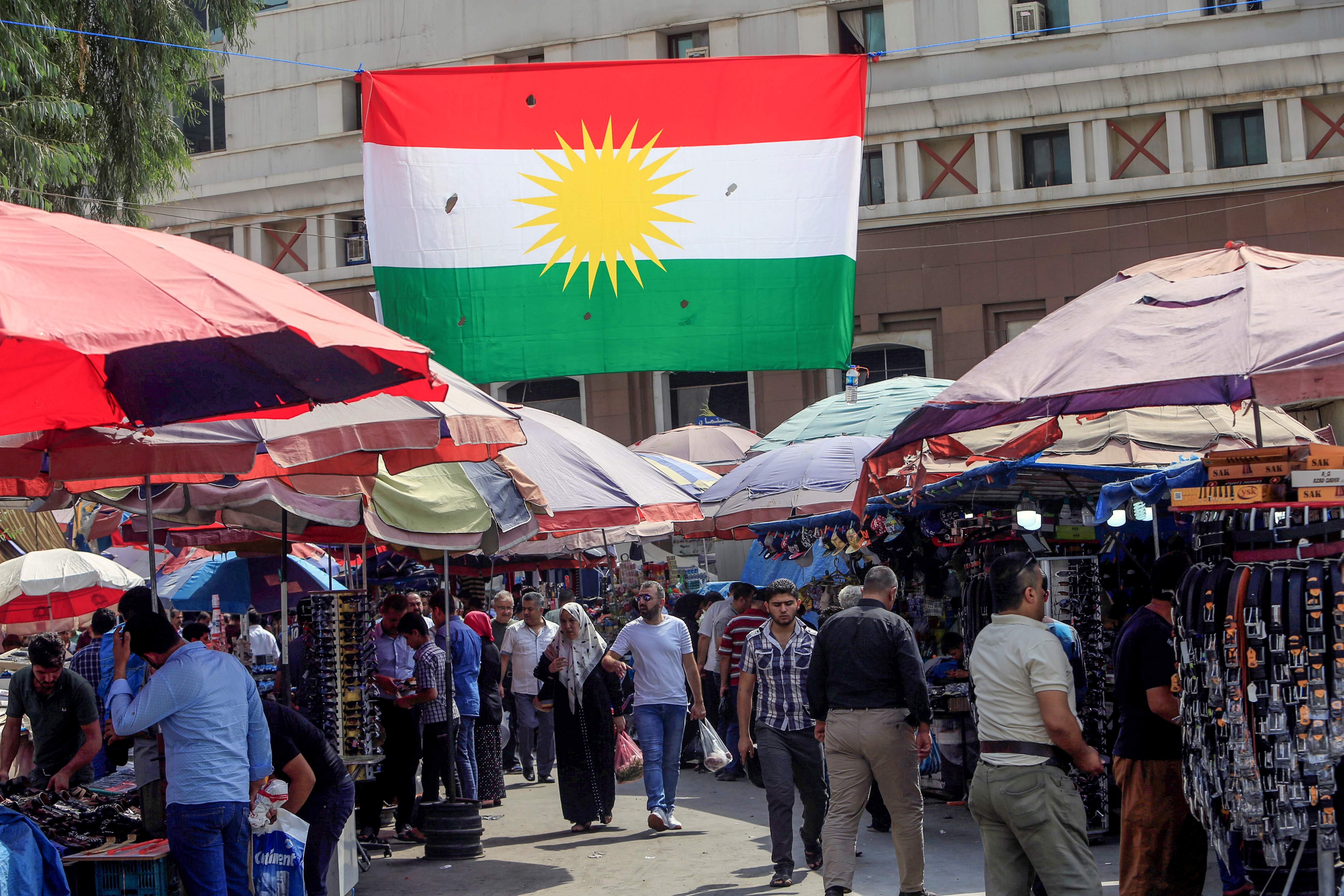People walk at a market, near a Kurdish flag in Erbil, Iraq