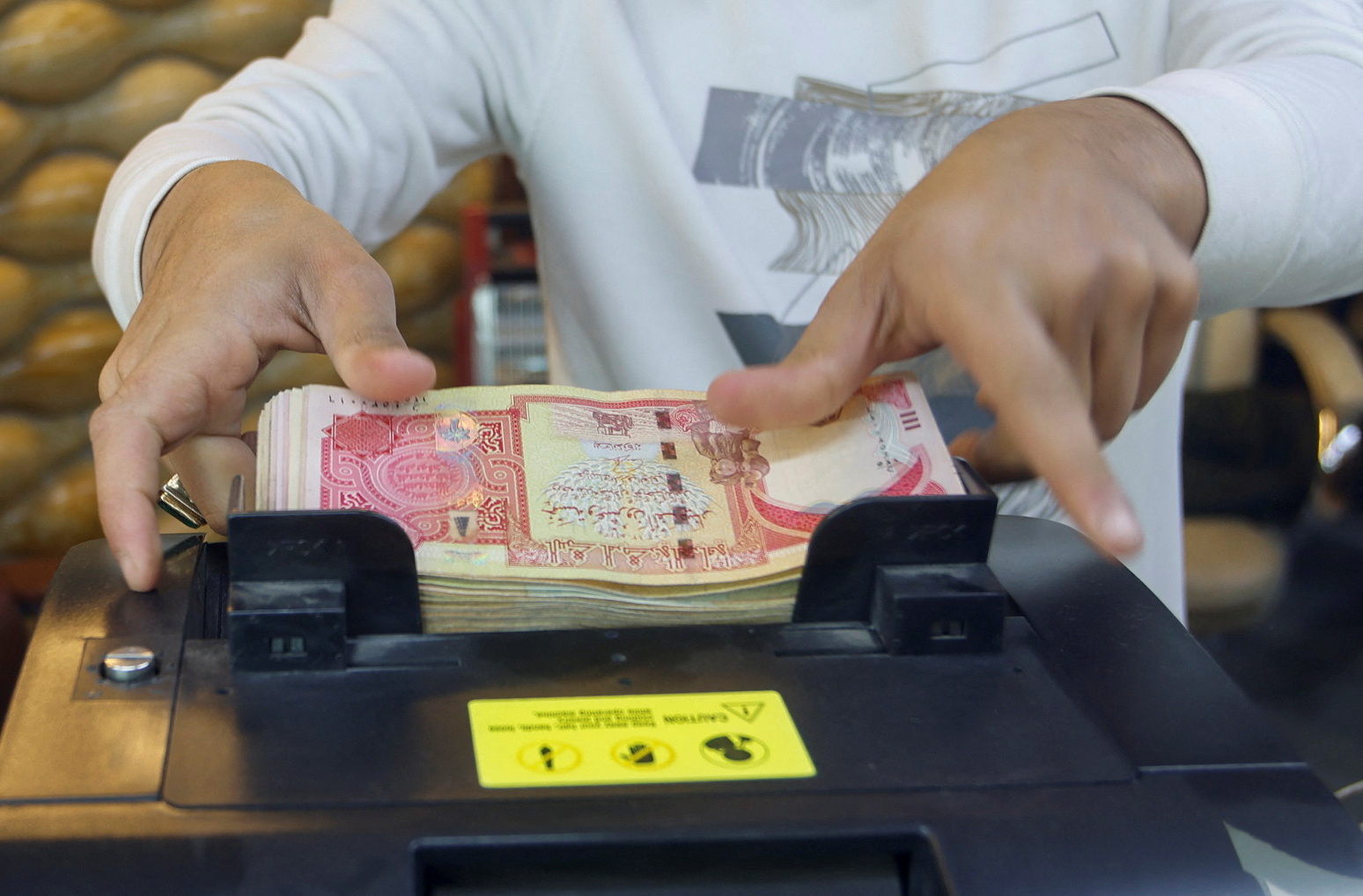 A man counts Iraqi dinars on a money counting machine at a currency exchange shop in Baghdad, Iraq, January 23, 2023. REUTERS/Ahmed Saad