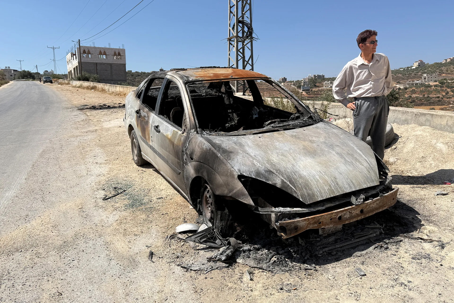 A Palestinian man stands next to a vehicle torched by Israeli settlers during a recent violent assault on the village of Jalud in the occupied West Bank [Al Jazeera]