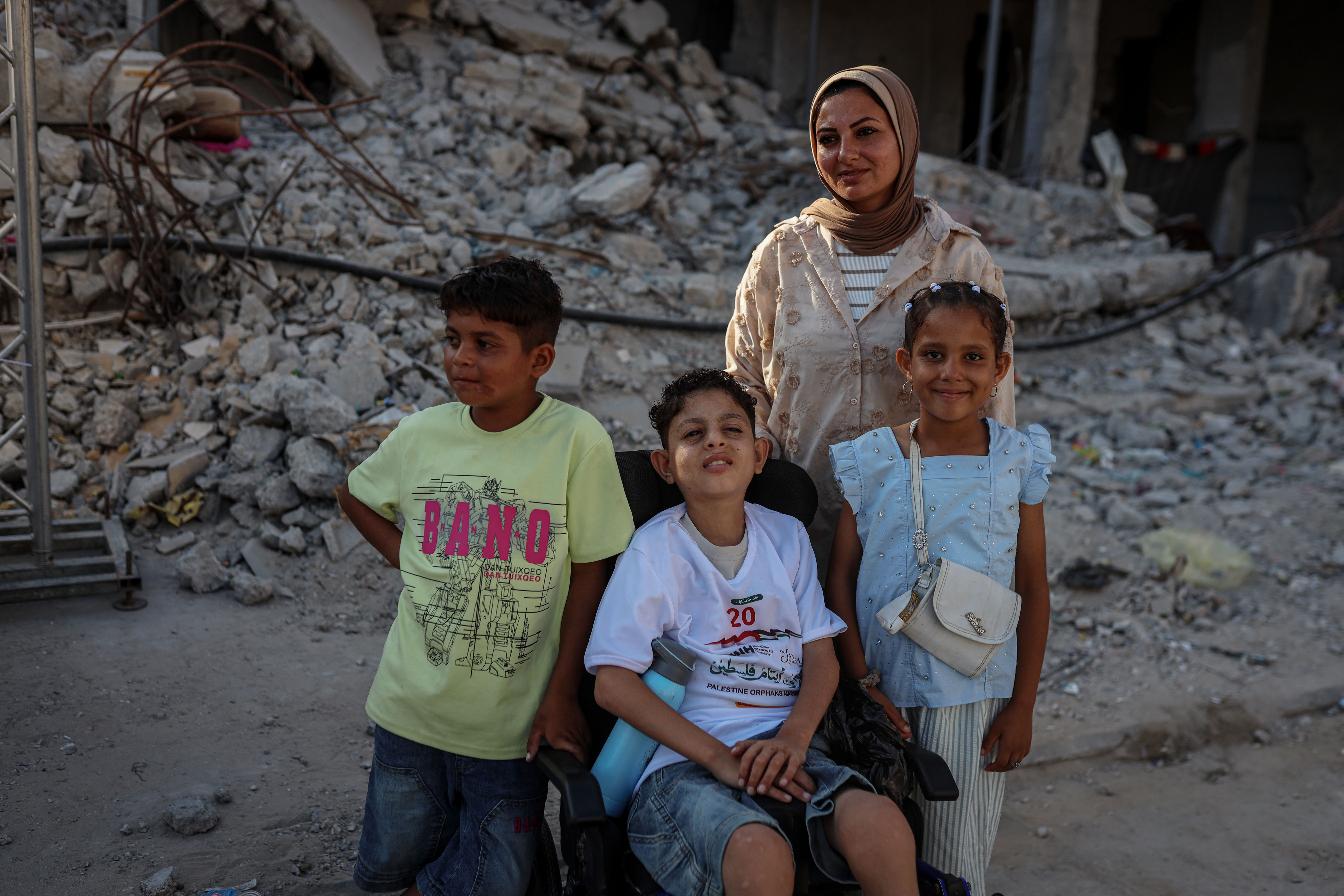 Warda Hijazi with her children: Saif, 13, who was severely injured and left paralysed during the war, her daughter Sarah, 9, and her son Ammar, 10 [Abdelhakim Abu Riash/ Al Jazeera]