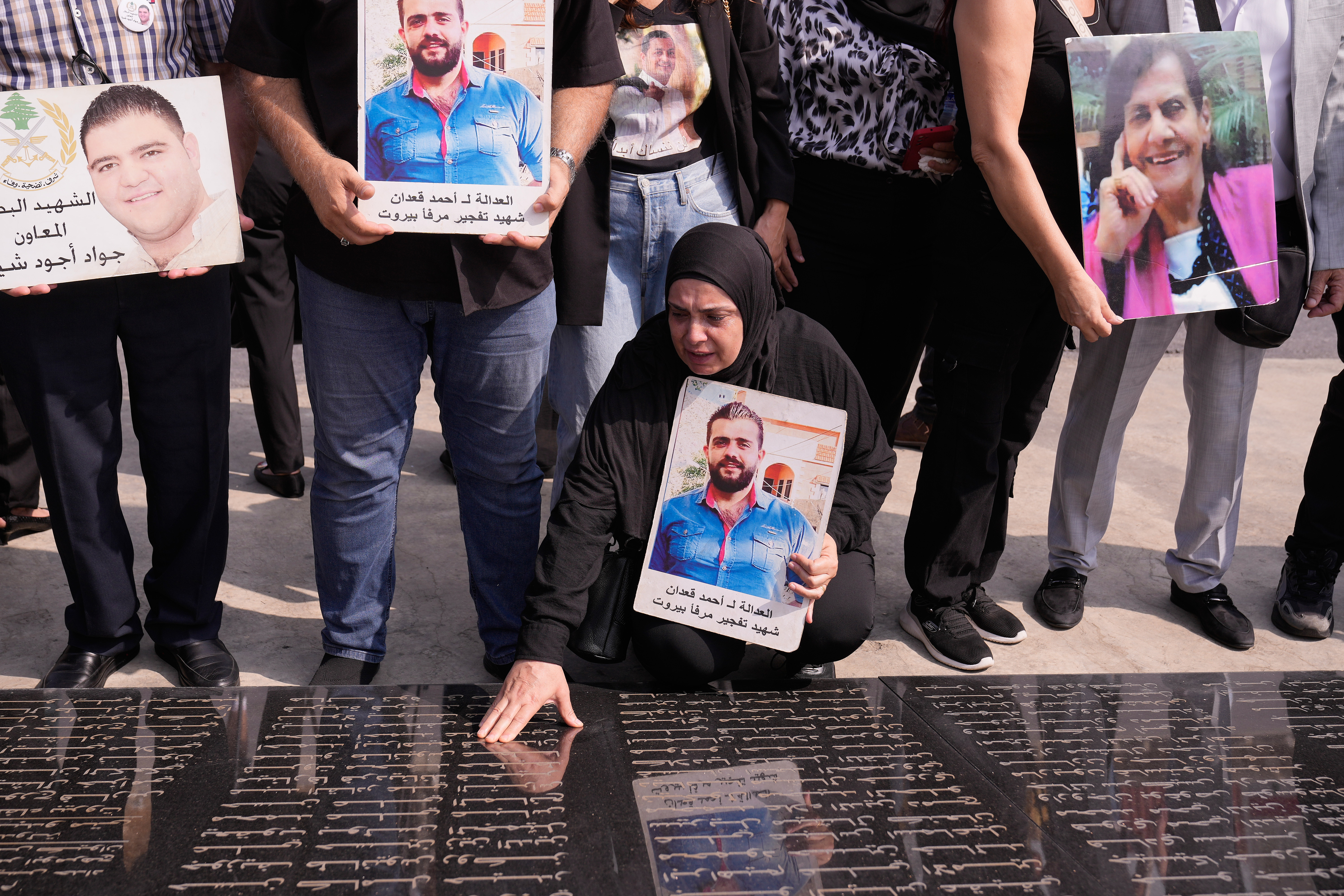 A woman cries as she holds a poster with a person's picture and points to a memorial stone.