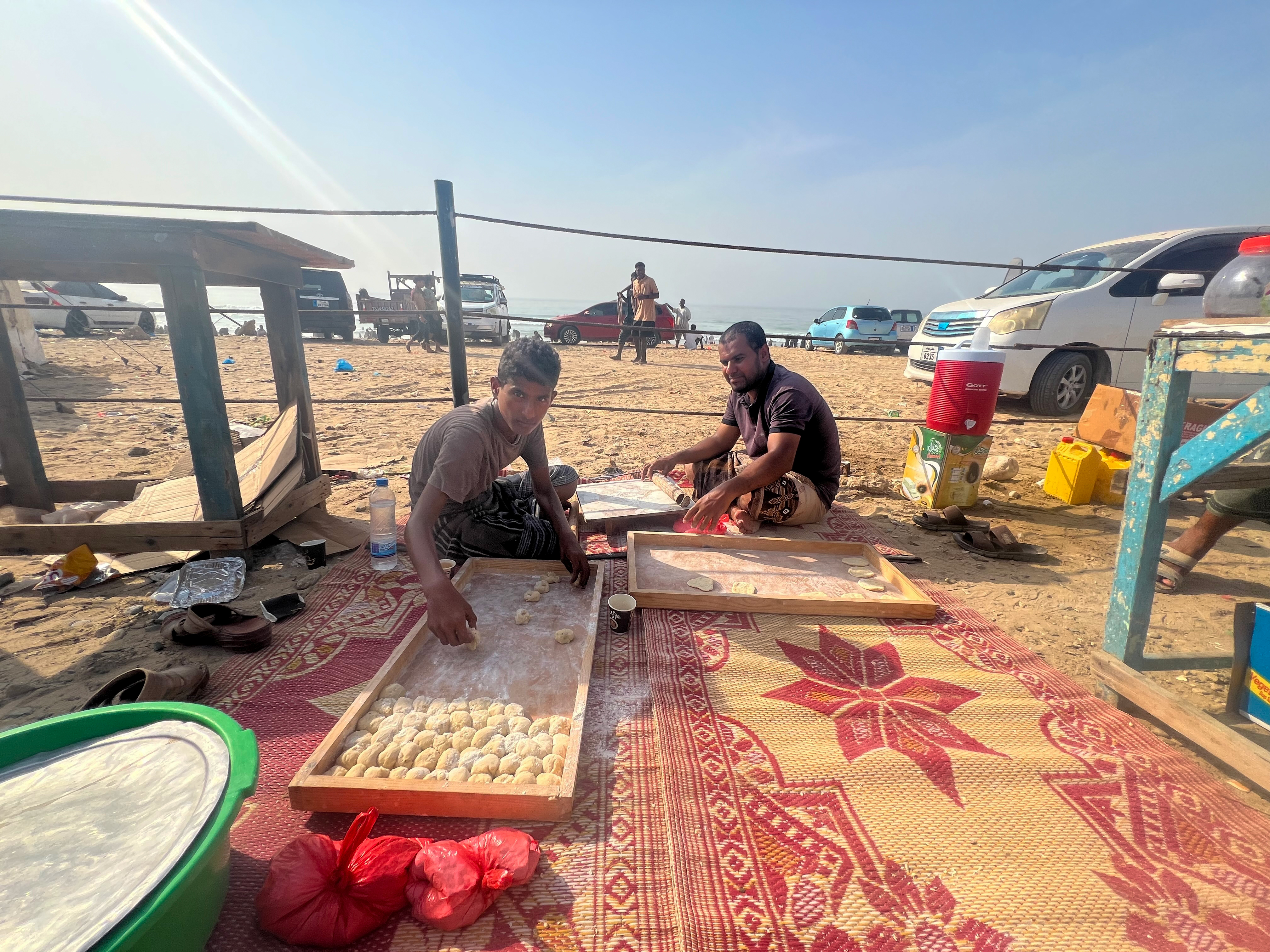 Abdulrahman Badr (left) and his friend prepare Bakhmari, a traditional flatbread, before serving it with tea and sambousa to beachgoers during the annual Al-Baldah season in Mukalla. [Saeed Al-Batati/Al Jazeera]