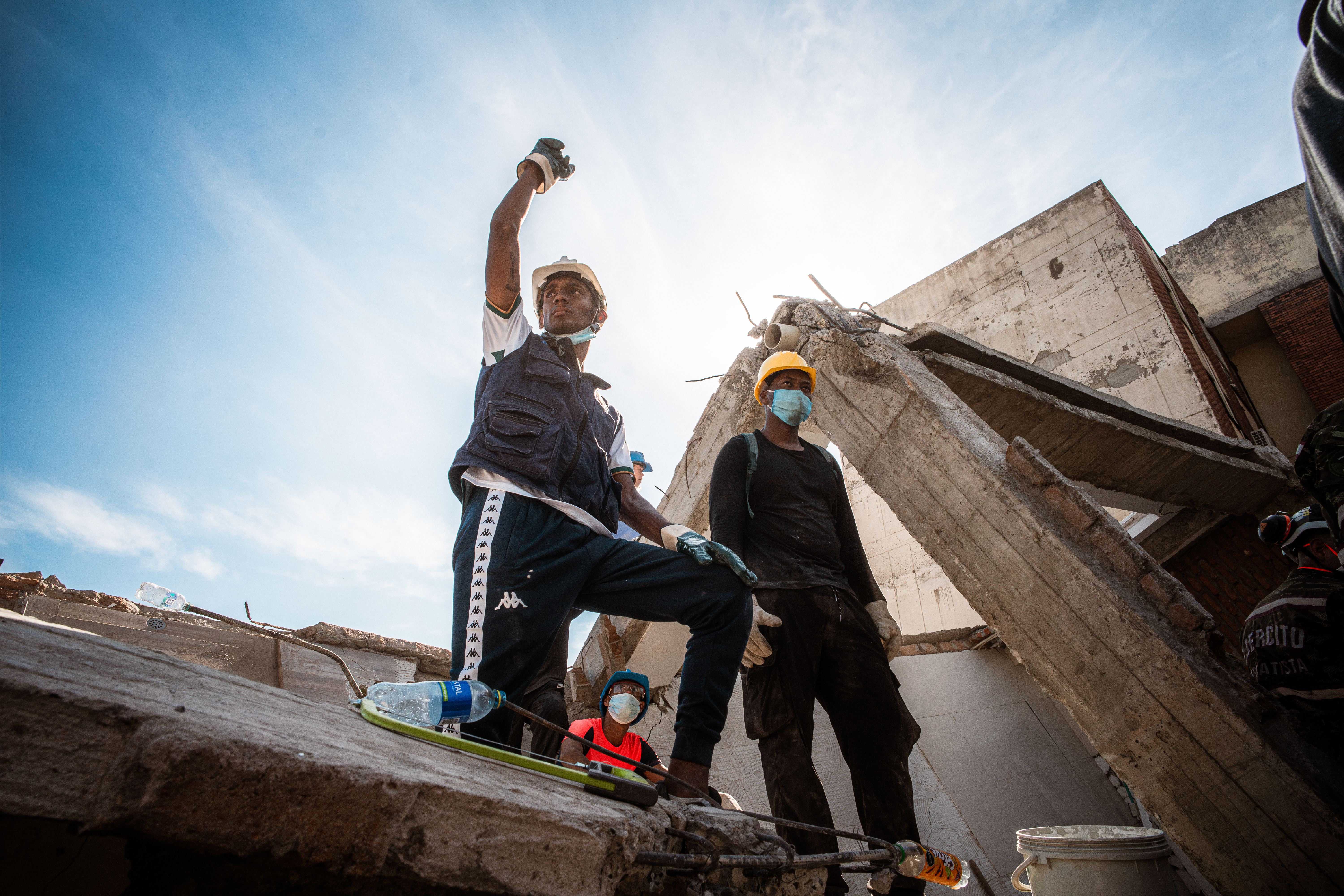 A volunteer signals for silence as rescuers attempt to locate survivors beneath the debris. [Euan Wallace / Al Jazeera]