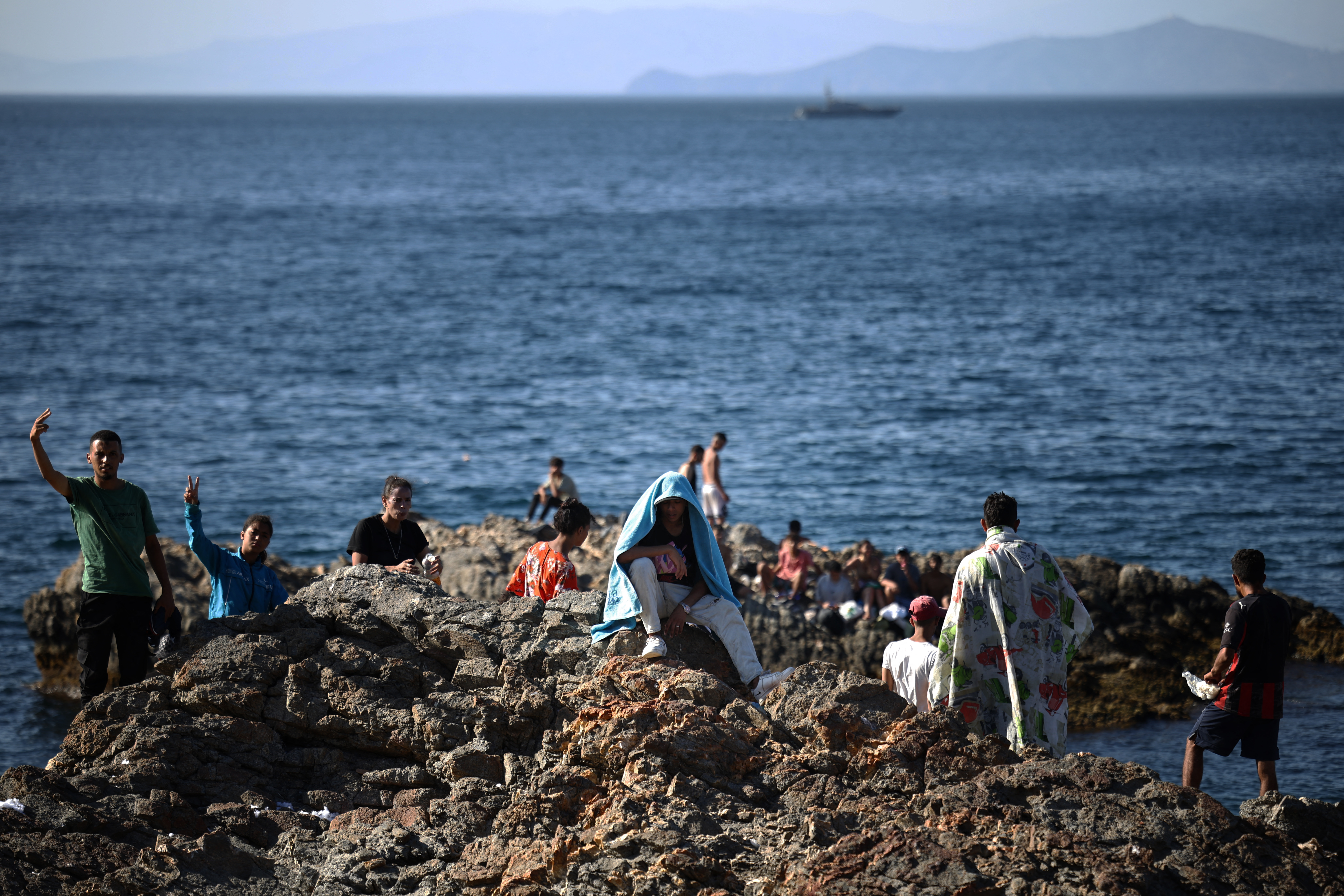 A group of migrants wave from the coastal rocks near the border post of the Spanish enclave of Ceuta