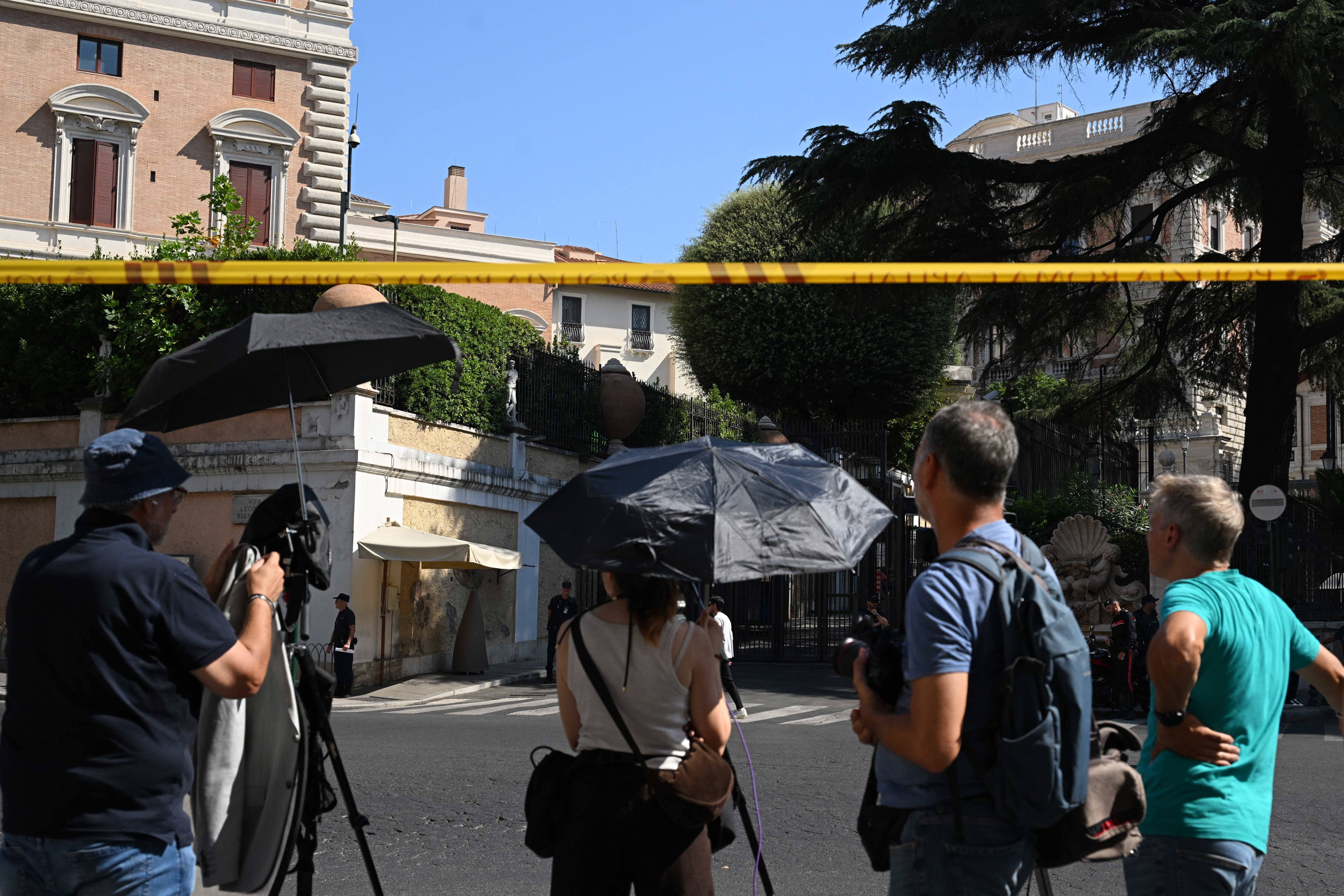 Journalists stand and wait in front of a building.