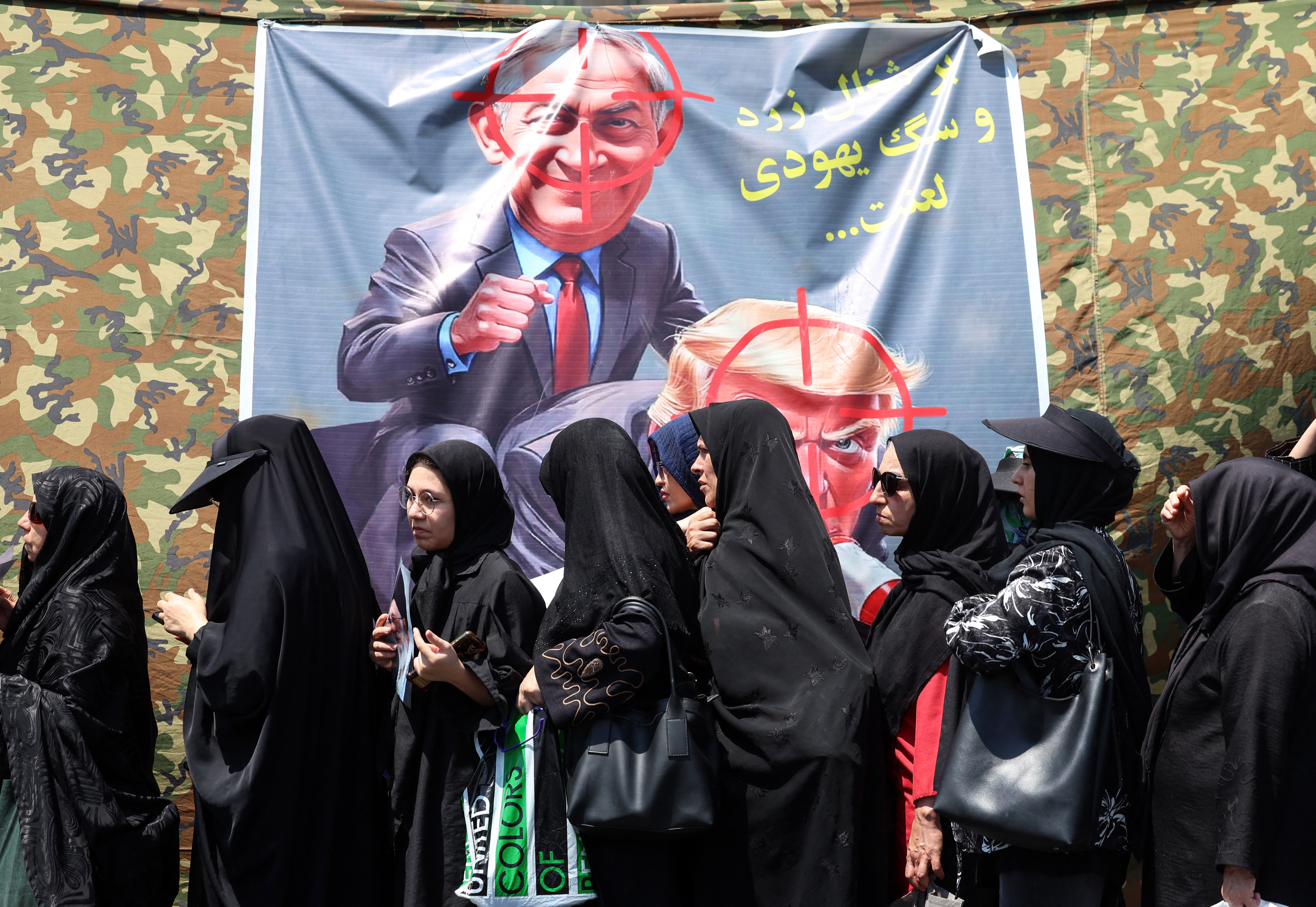 Shia Muslim devotees walk past a banner calling for revenge against the US president and the Israeli prime minister.
