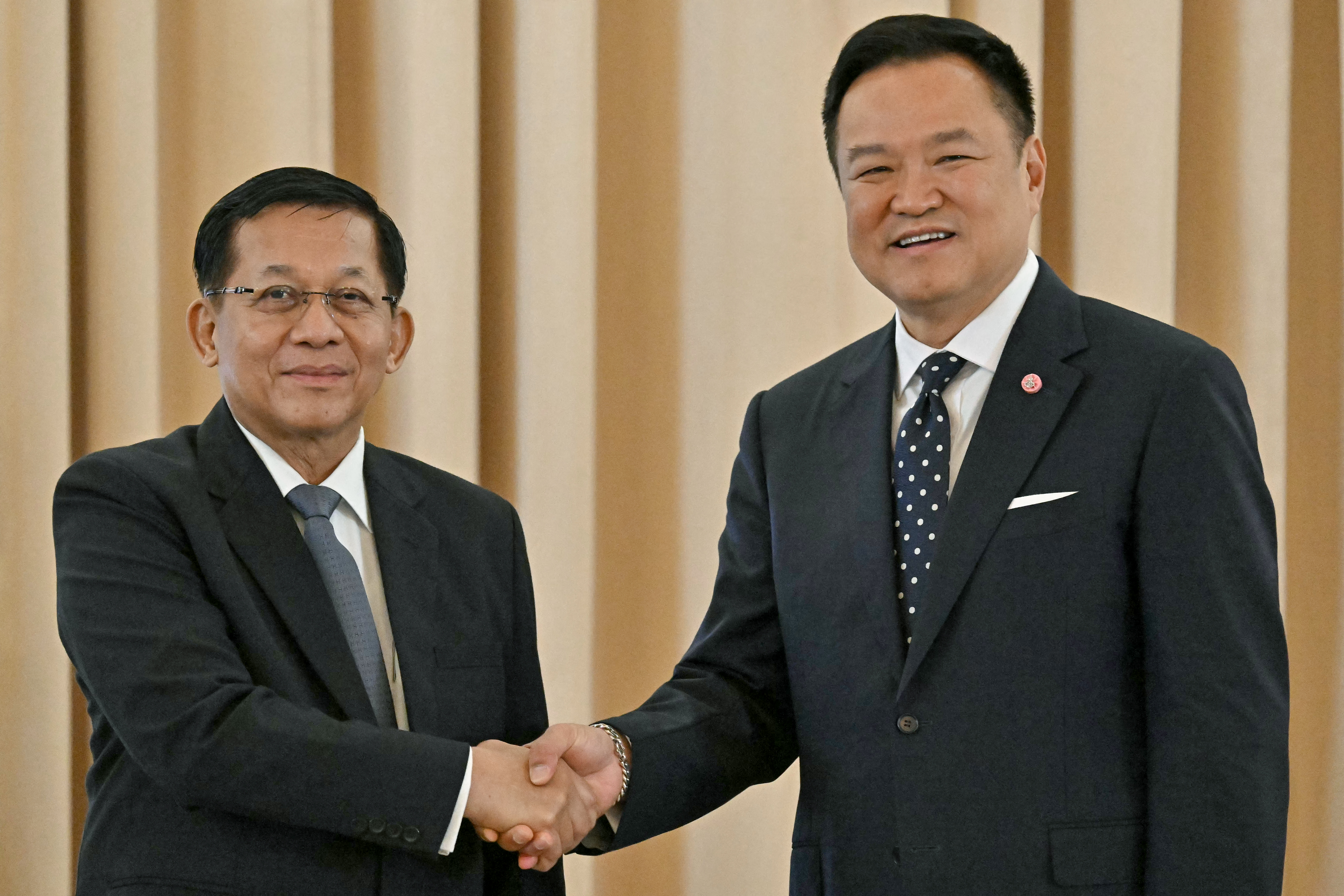 Myanmar's President Min Aung Hlaing (L) and Thailand's Prime Minister Anutin Charnvirakul shake hands and smile at the camera.
