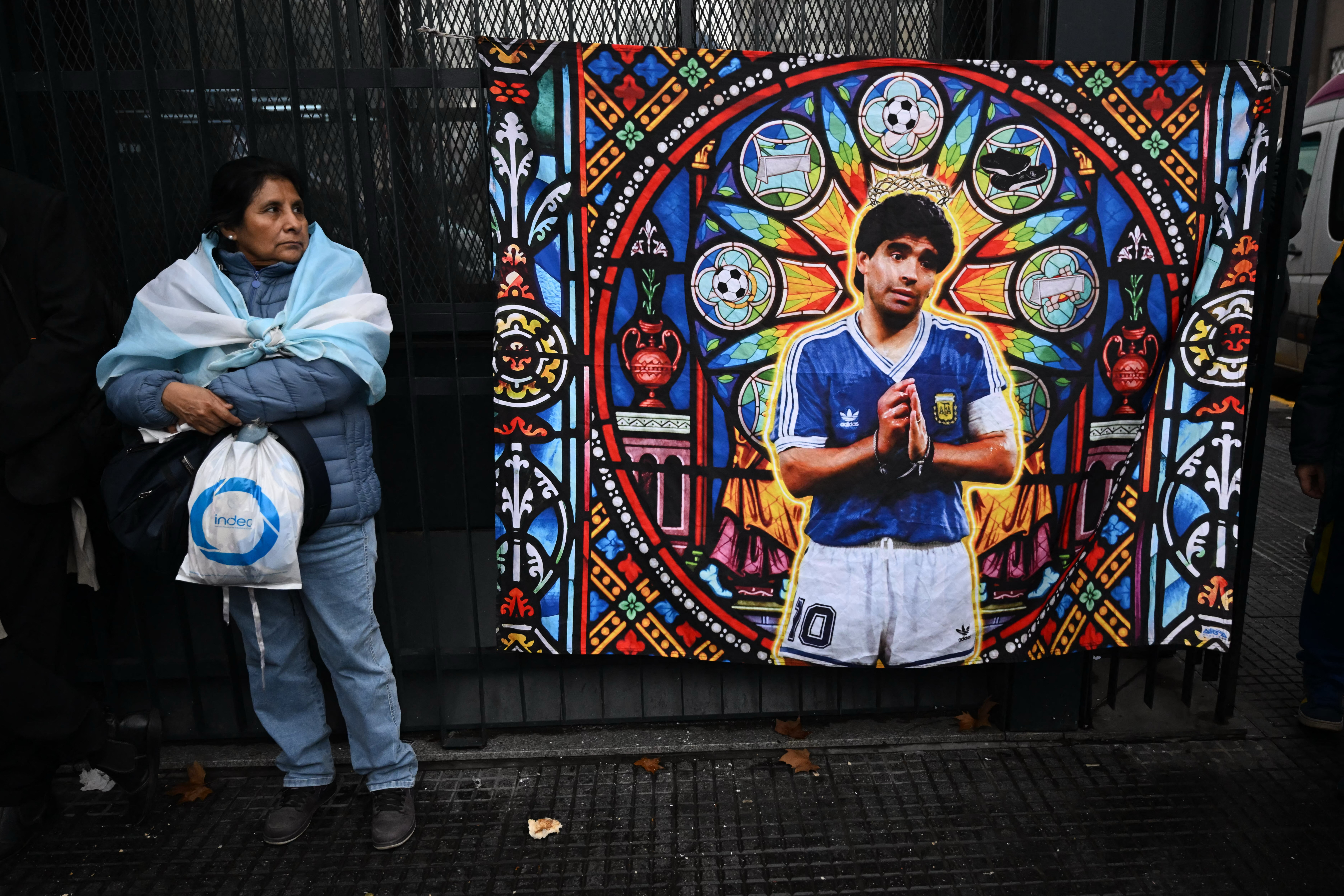 A woman stands next to a banner depicting late Argentine football legend Diego Maradona outside the National Congress in Buenos Aires on August 6, 2026, as senators debate a bill on the inviolability of private property. (Photo by Luis ROBAYO / AFP)