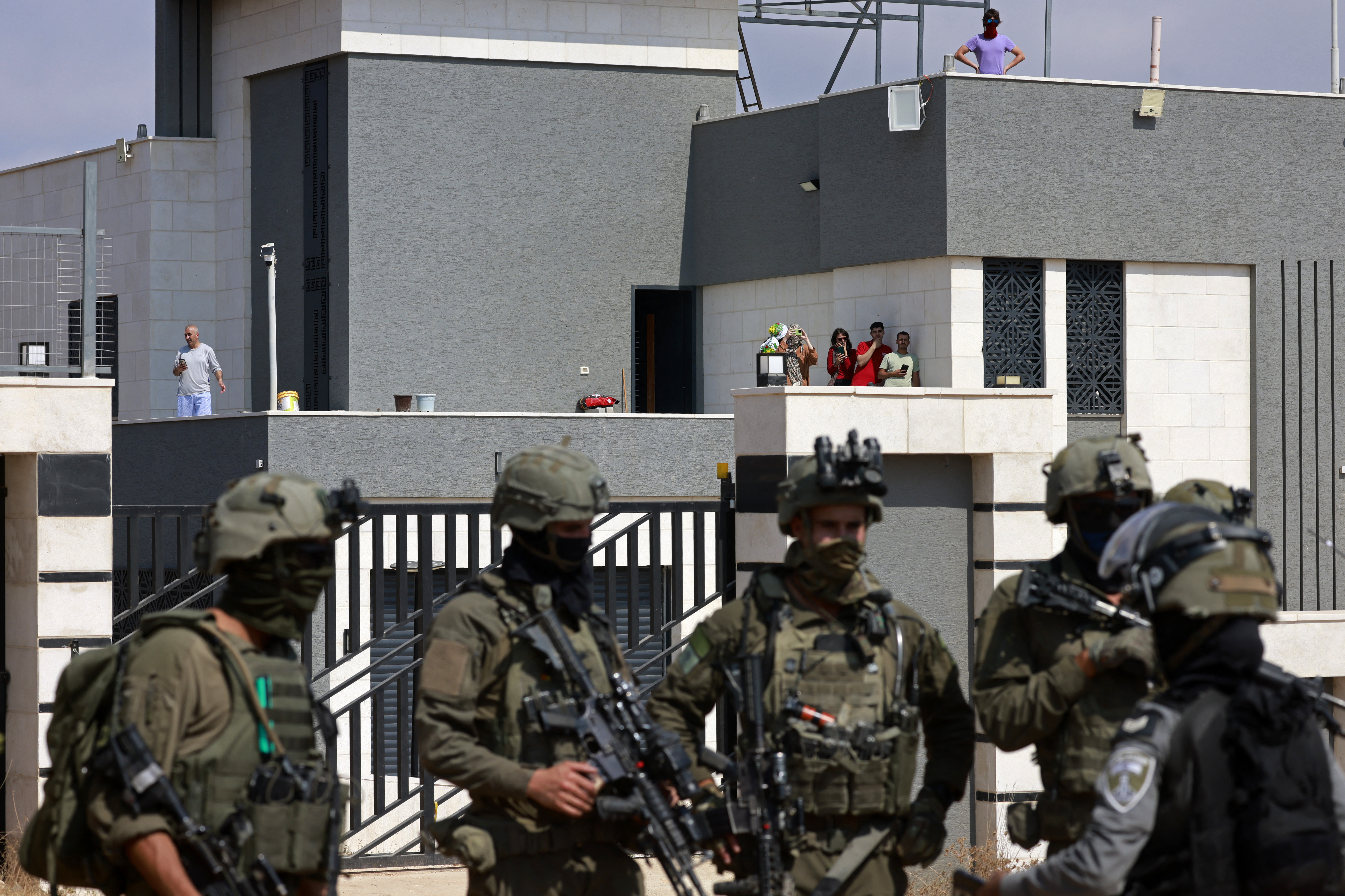 Israeli soldiers stand in front of the entrance of a besieged Palestinian house by Israeli settlers in the village of Qusra, south of Nablus, in the occupied West Bank, on August 14, 2026.