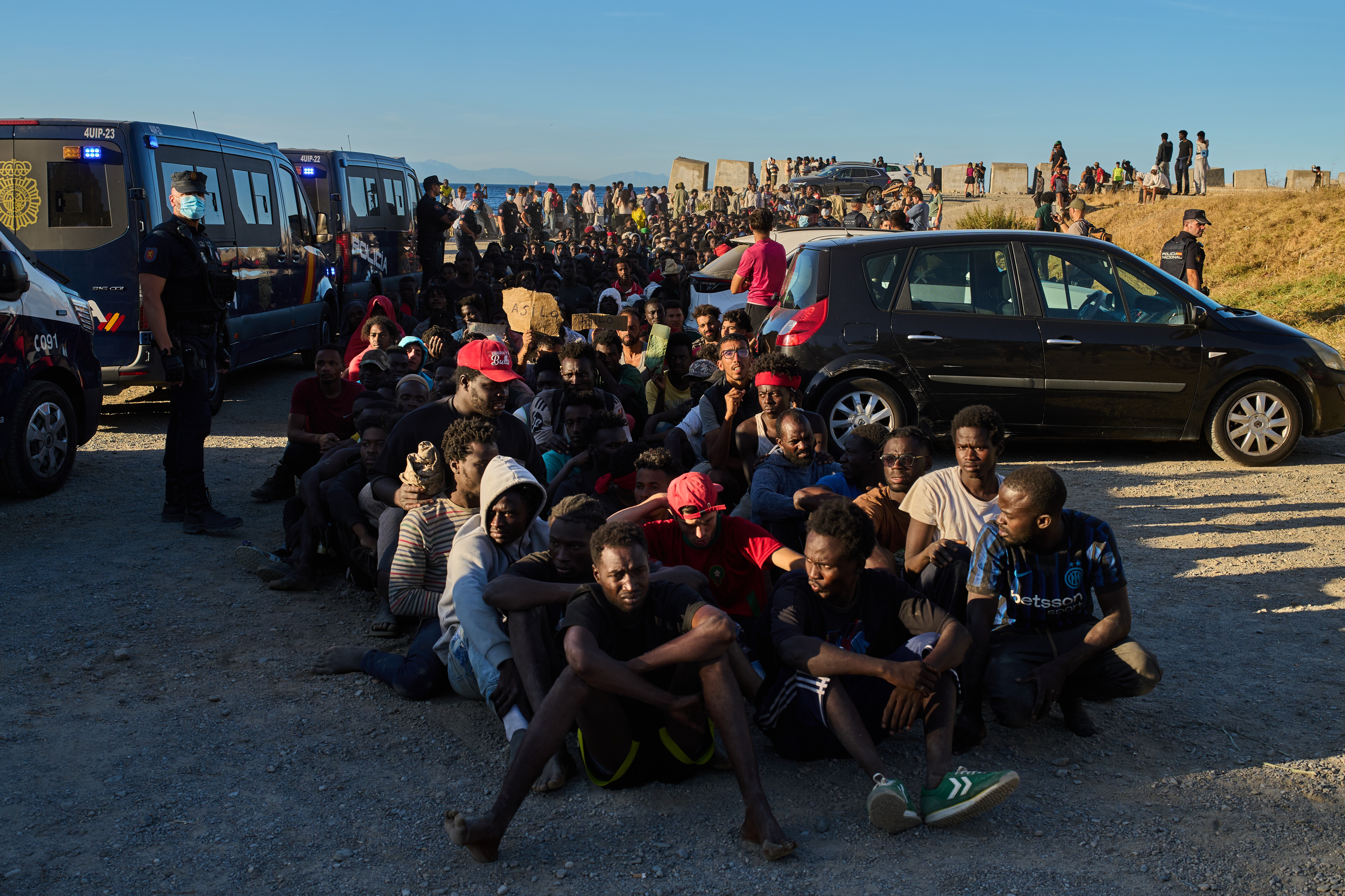 Migrants who crossed from Morocco into Spain line up for food distribution on a beach in the Spanish enclave of Ceuta, Monday, Aug. 3, 2026. (AP Photo/Bernat Armangue)