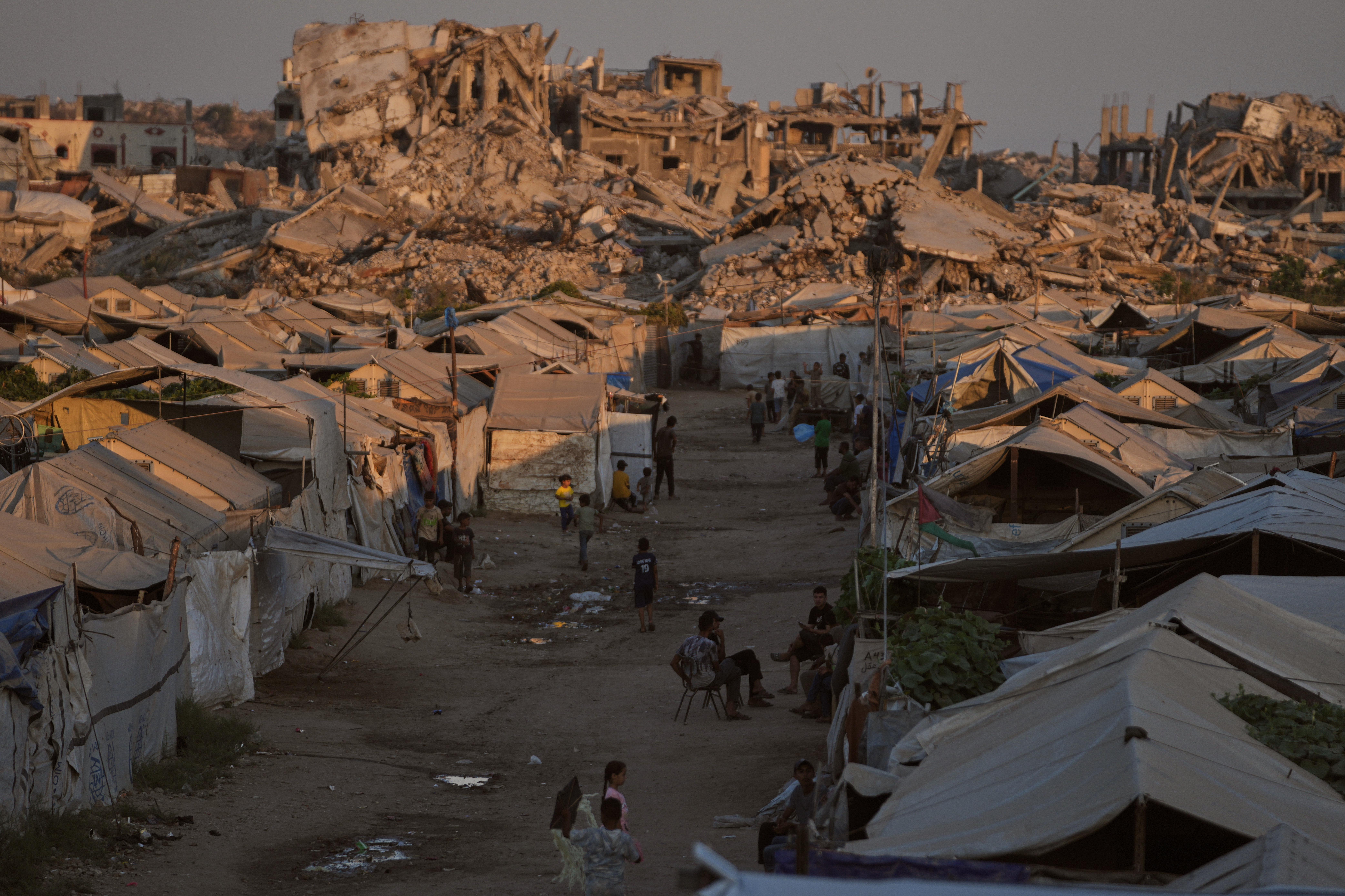 People walk past tents sheltering displaced Palestinians amid the ruins left by the Israeli air and ground offensive in Gaza City, Monday, Aug. 10, 2026. (AP Photo/Jehad Alshrafi)