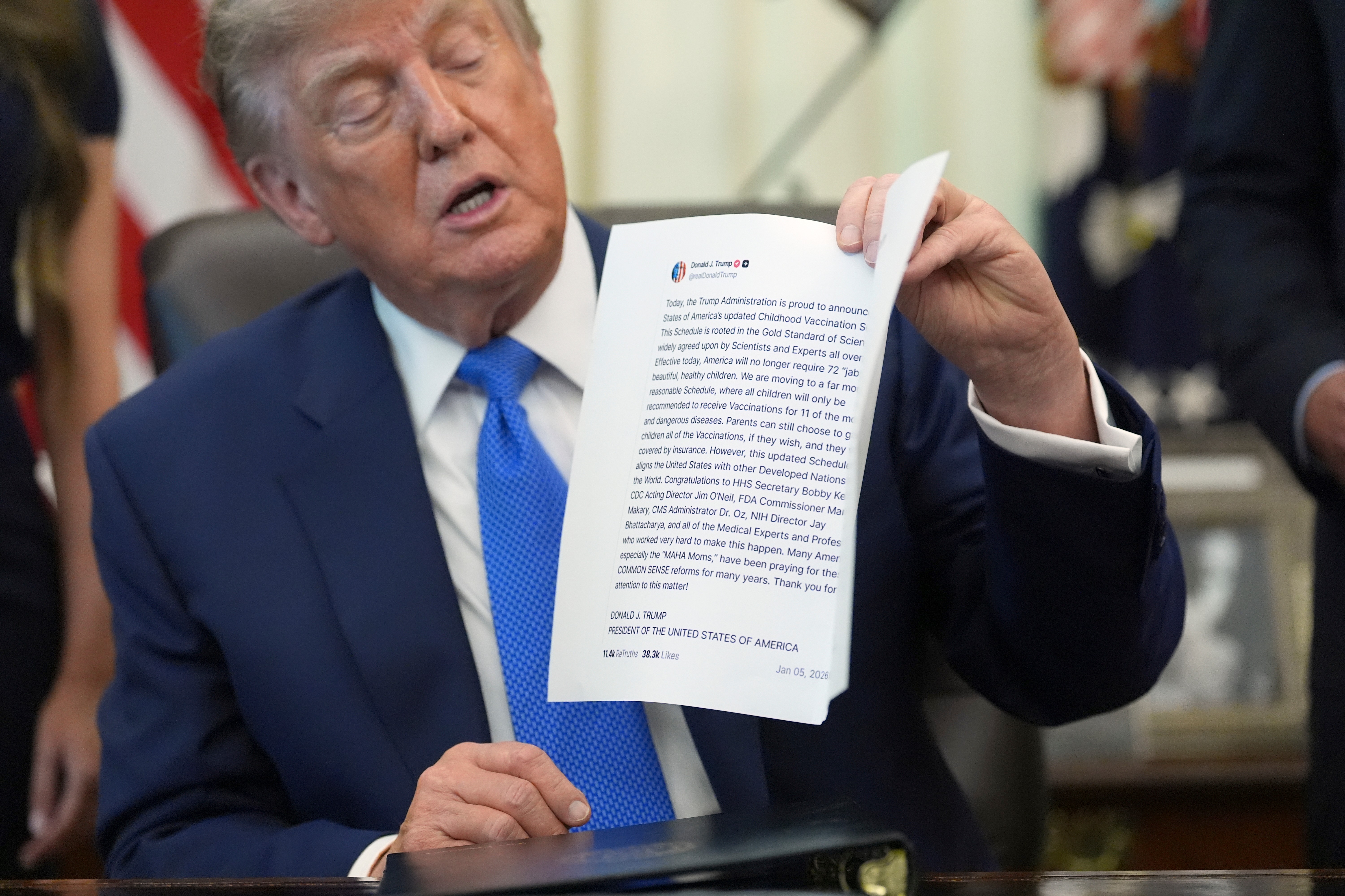 President Donald Trump holds up an image taken from his Truth Social account during a meeting to sign an executive order about vaccines, Monday, Aug. 10, 2026, in the Oval Office of the White House in Washington. (AP Photo/Jacquelyn Martin)
