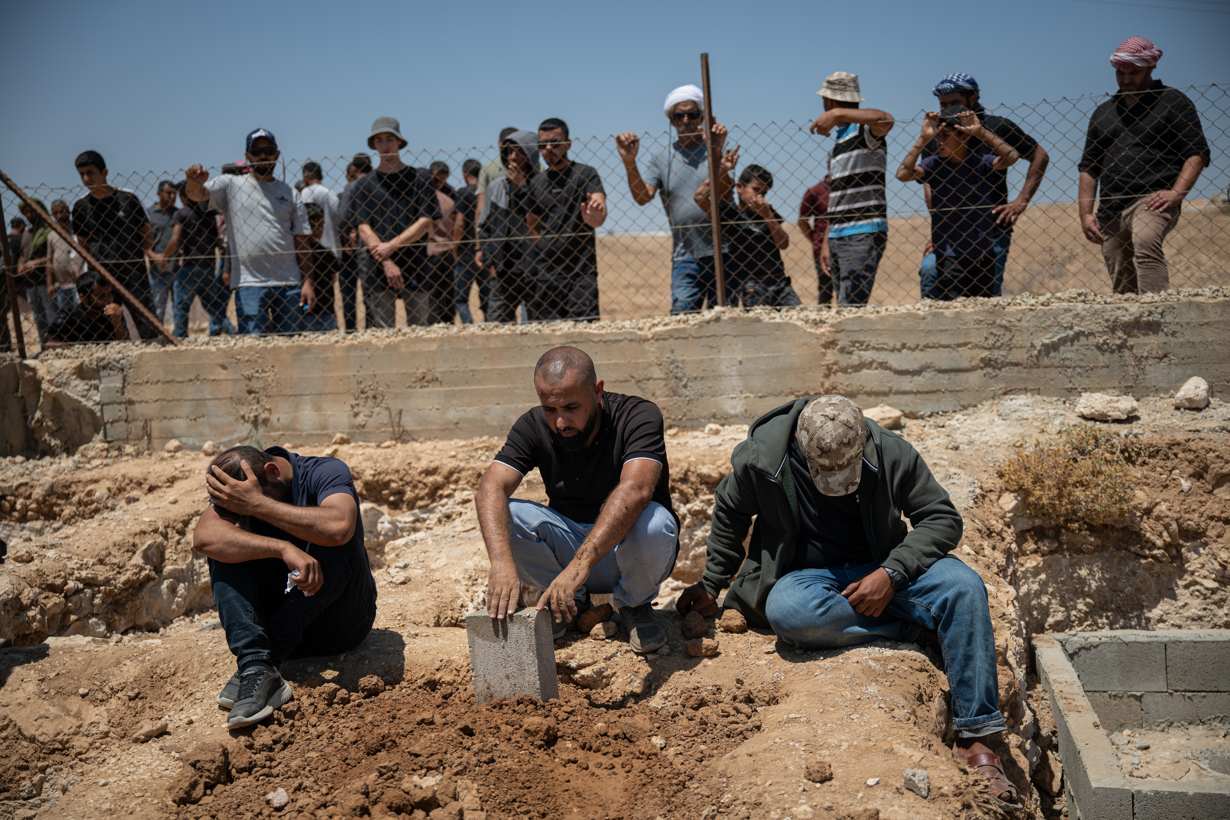 UMM AL-KHEIR, WEST BANK - AUGUST 7: Family and friends of Awdah Hathaleen look on at his grave moments after his burial on August 7, 2025 in Umm al-Kheir, West Bank. The 31-year-old Palestinian activist and father of three was killed on July 28 when Israeli settler Yinon Levi allegedly opened fire during a confrontation in the Bedouin village of Umm al-Kheir (or Umm al-Khair), in the Masafer Yatta region of the occupied West Bank. A group of local women had gone on hunger strike to demand an unconditional release of Hathaleen's body, as well as the release of several people who were detained by Israeli forces following the shooting incident. Levi, who is sanctioned by the UK, EU, and previously by the US, was temporarily detained on house arrest following Hathaleen's death. Hathaleen was known for his work on the Oscar-winning film 'No Other Land,' which documents the Israeli demolition of Palestinian homes in Masafer Yatta. (Photo by Tamir Kalifa/Getty Images)