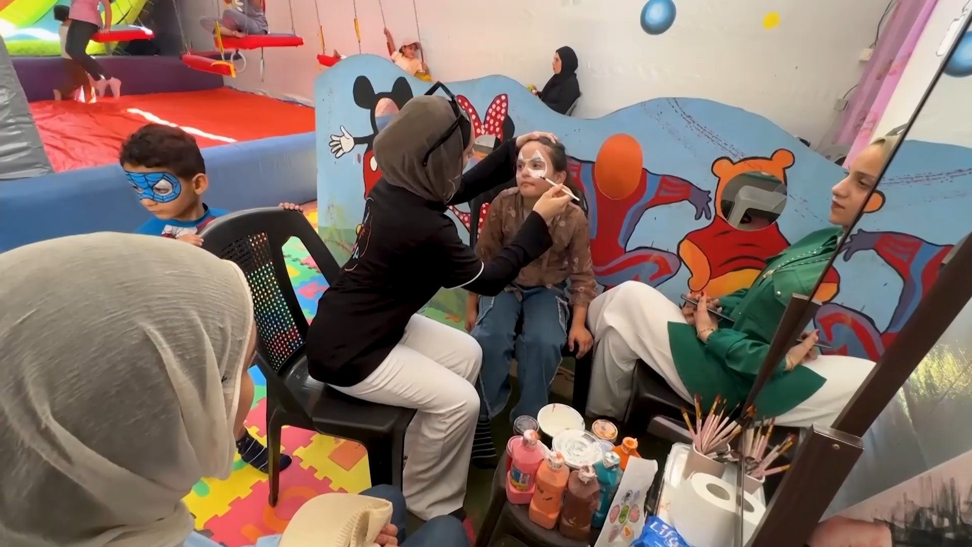 A woman paints a child's face at the 'Jump City' indoor play center in northern Gaza. GAZA CITY, AUGUST 3, 2026 [Screenshot from Viory file]