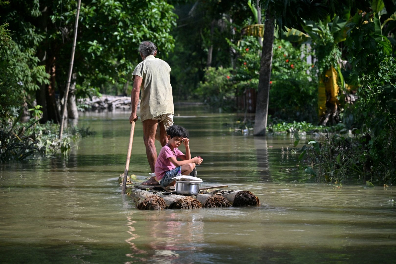 A girl and her grandfather travel on a raft through floodwaters following heavy monsoon rains at a village in Assam's Sivasagar district on July 27, 2026. [Biju BORO/AFP]