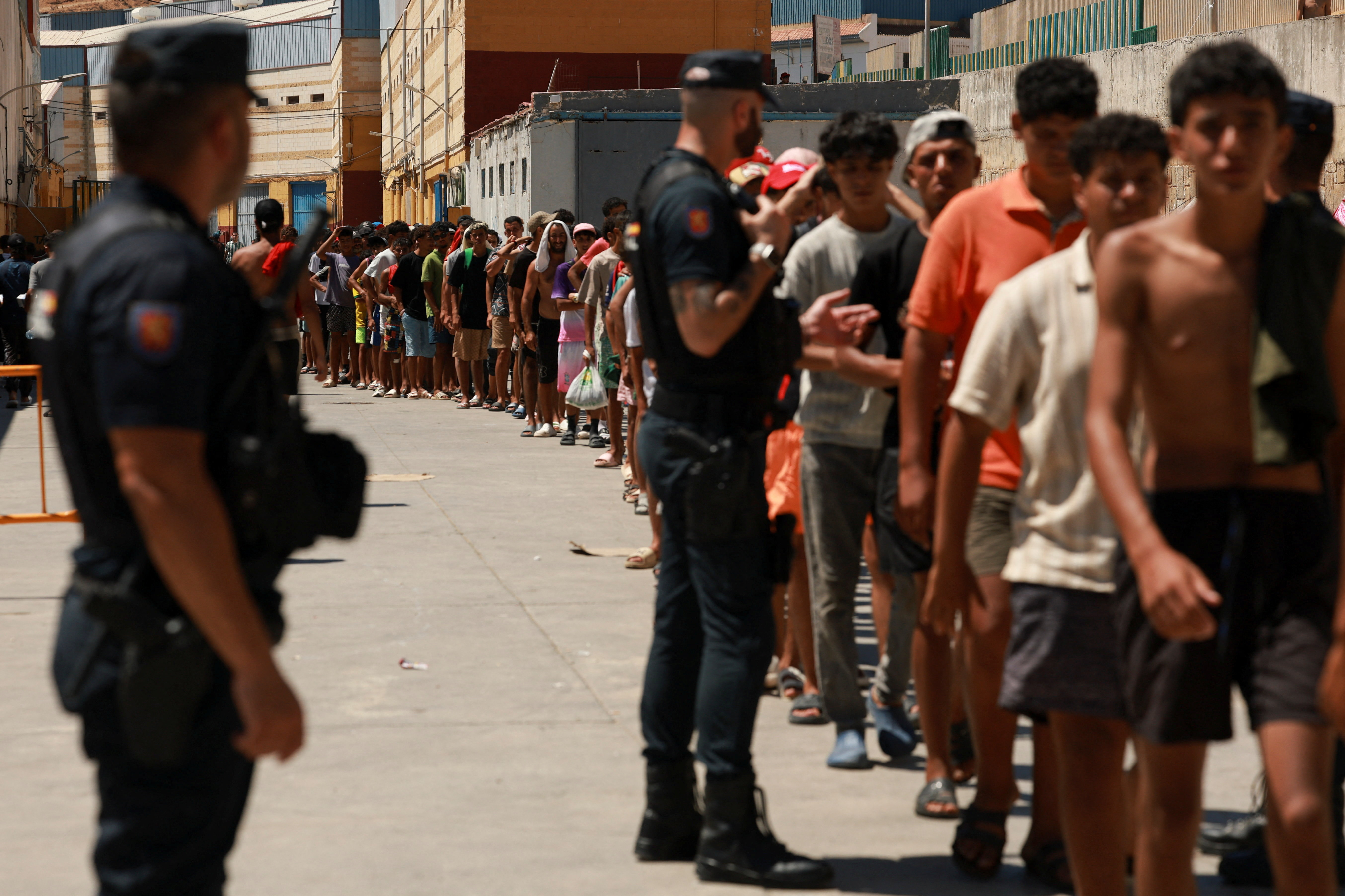 Migrants queue to receive food staples from local NGO Media Luna Blanca in an industrial area where they are sleeping amid recent mass crossings by migrants on foot and by sea from Morocco into the Spanish territory, in Ceuta, Spain, August 6, 2026. REUTERS/Violeta Santos Moura