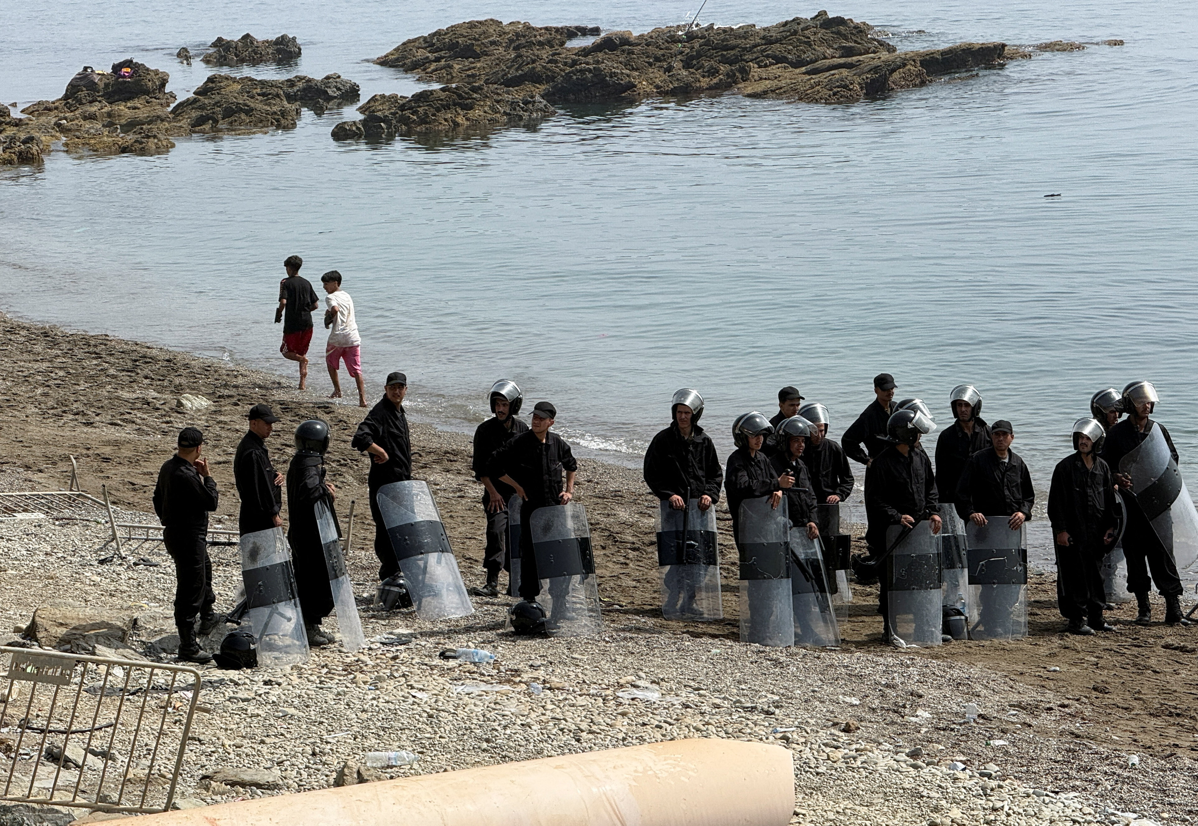 Security forces stand guard in Fnideq, Morocco, August 1, 2026, as migrants gather after crossing from the Spanish enclave of Ceuta to the Moroccan side of the border. Picture taken using a mobile phone. REUTERS/Stringer