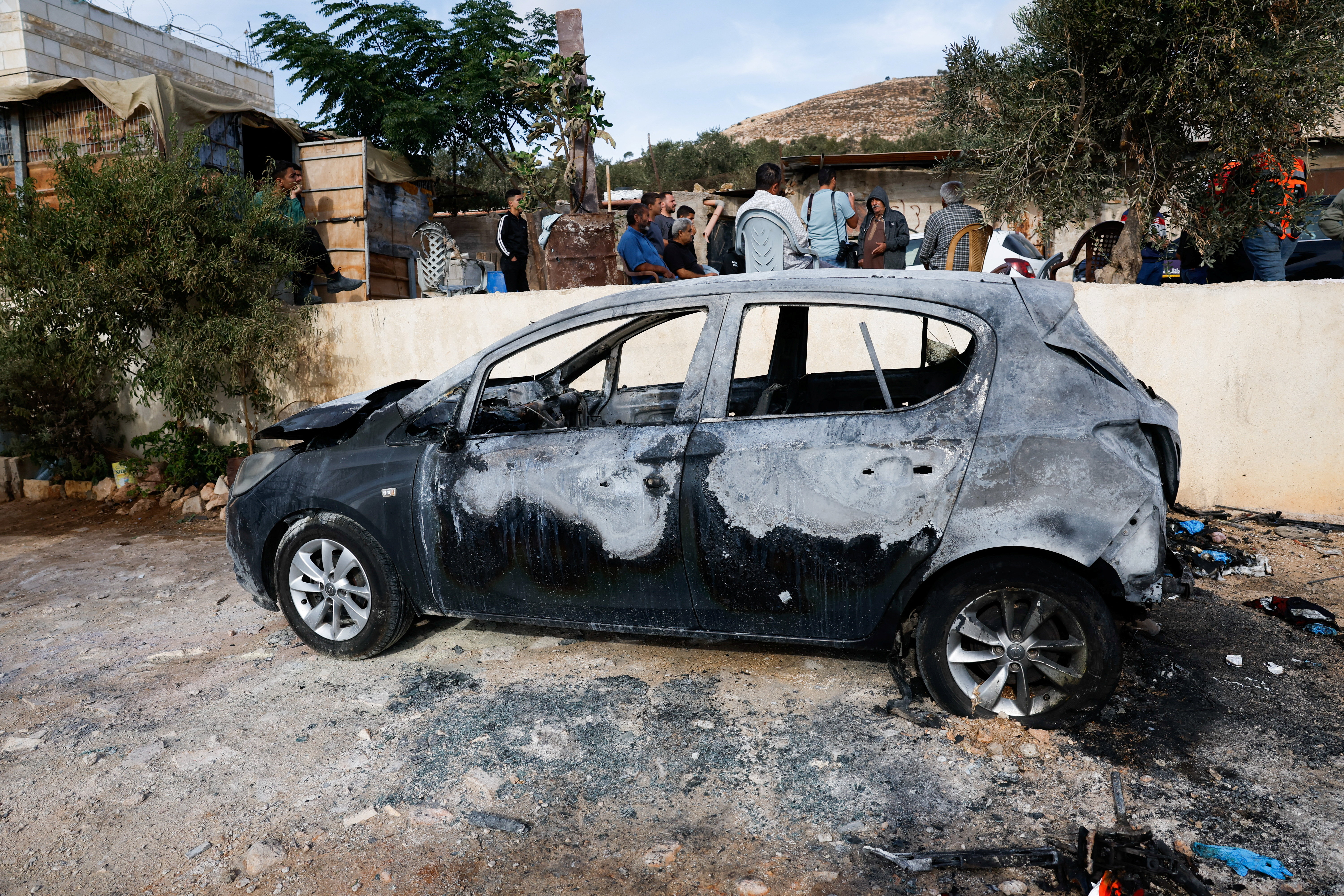 Palestinians sit near a vehicle damaged in what they say was an Israeli settlers attack, in Al-Mughayyir