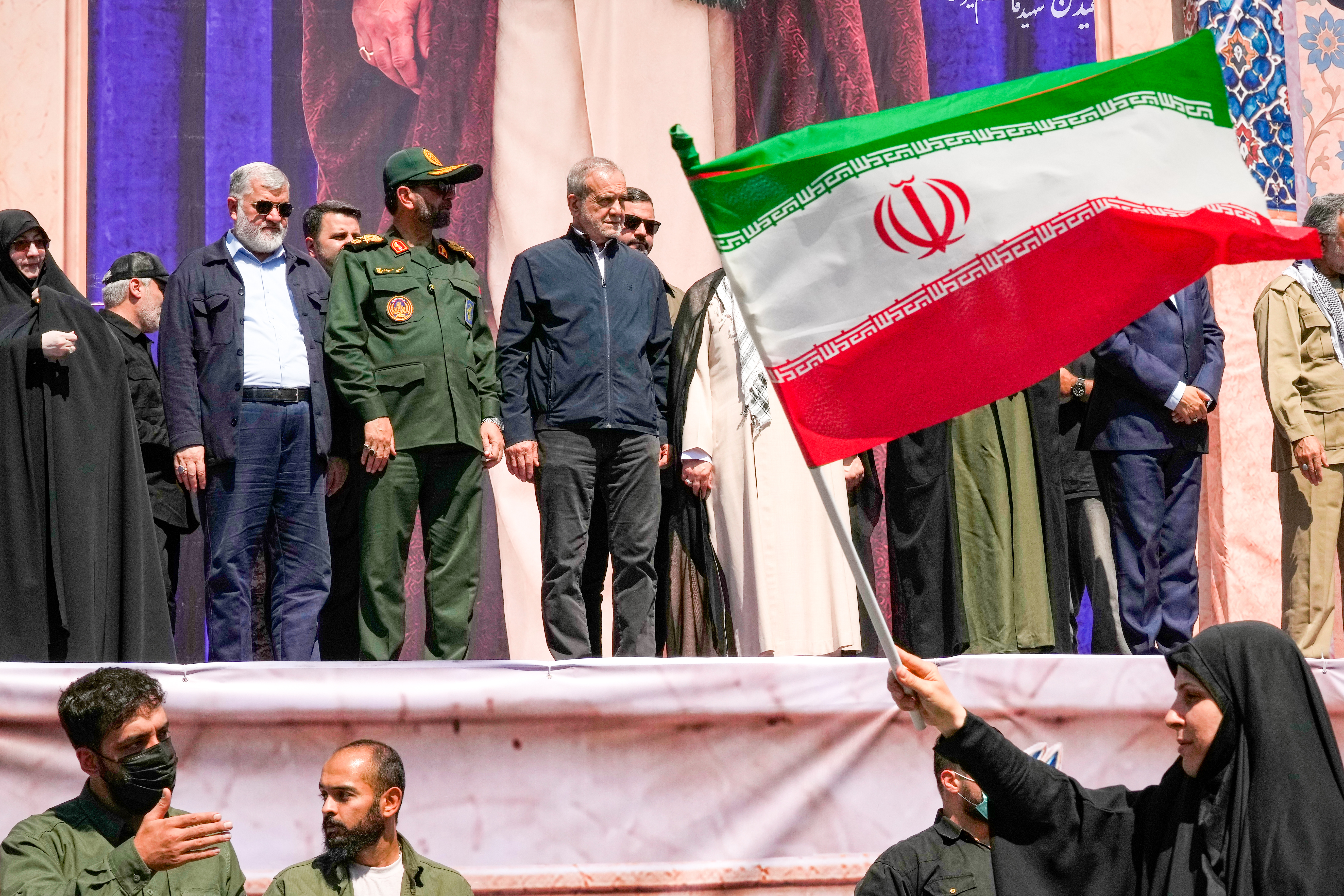 Iranian President Masoud Pezeshkian and other officials watch as a woman waves an Iranian flag during the state-organised "Janfada," or "Sacrifice for Iran," military-style parade in Tehran, Iran, on September 18, 2026 [Vahid Salemi/AP Photo]