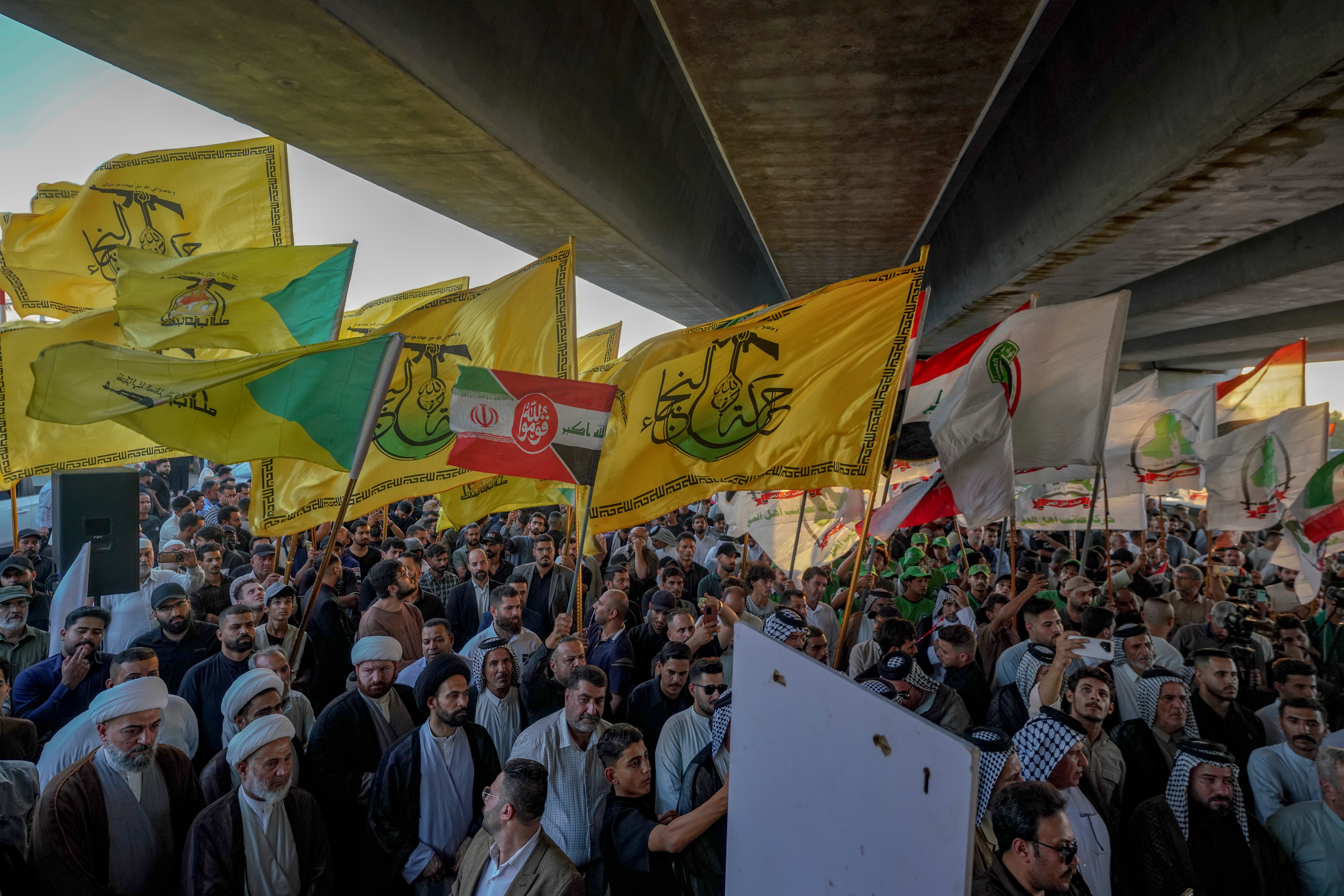Demonstrators wave flags, including those of the Iran-aligned Iraqi militia Harakat Hezbollah al-Nujaba, during a protest against the suspension of flights between Iraq and Iran outside Najaf International Airport in Najaf, Iraq, Monday, Sept. 28, 2026. (AP Photo/Anmar Khalil)