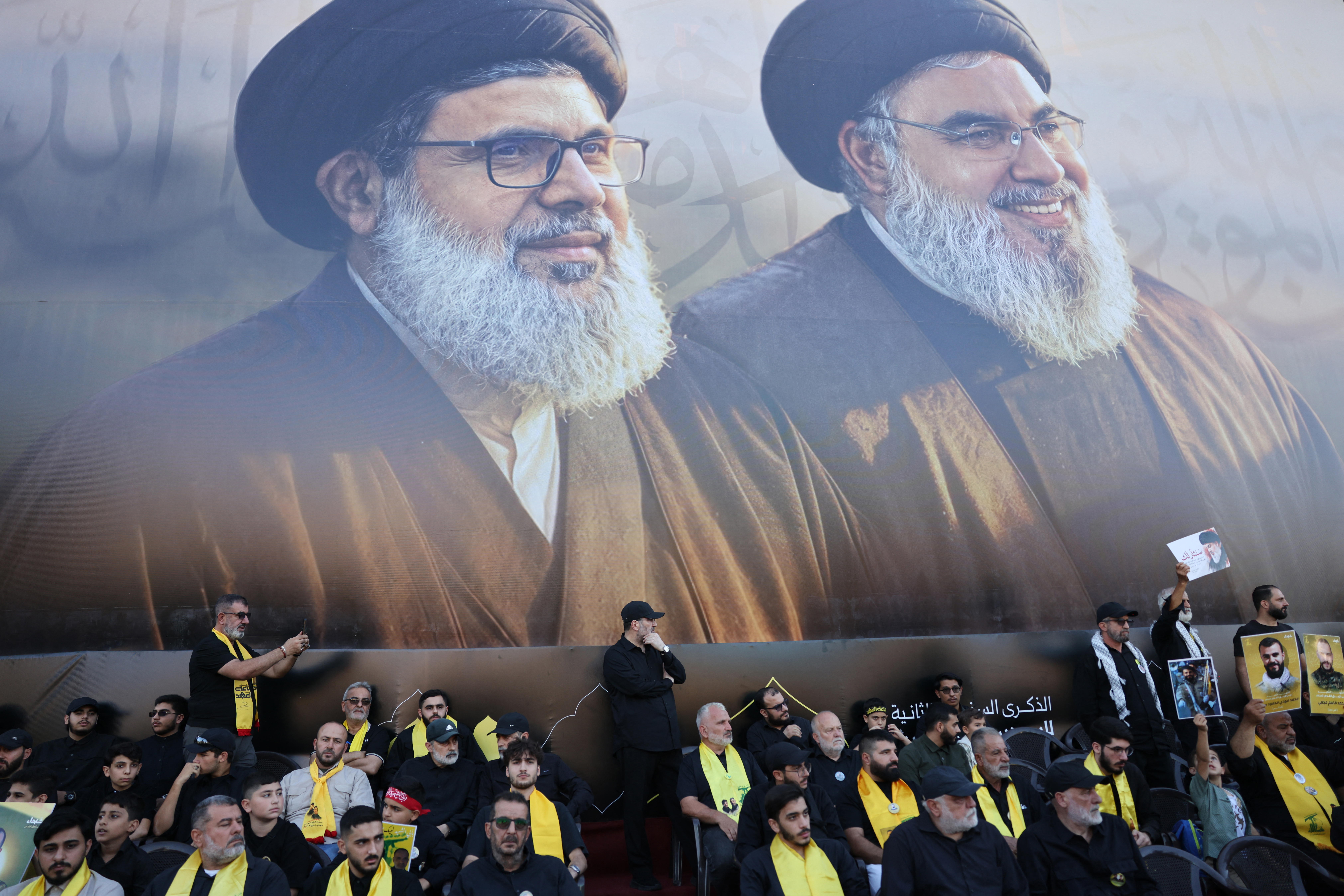 Supporters of Lebanese Shia movement Hezbollah sit underneath a big portrait of slain leaders Hassan Nasrallah (R) and Hashem Safieddine during a ceremony held to mark the second anniversary of Nasrallah's killing in a strike by Israel, in Beirut's southern suburbs on September 27, 2026.