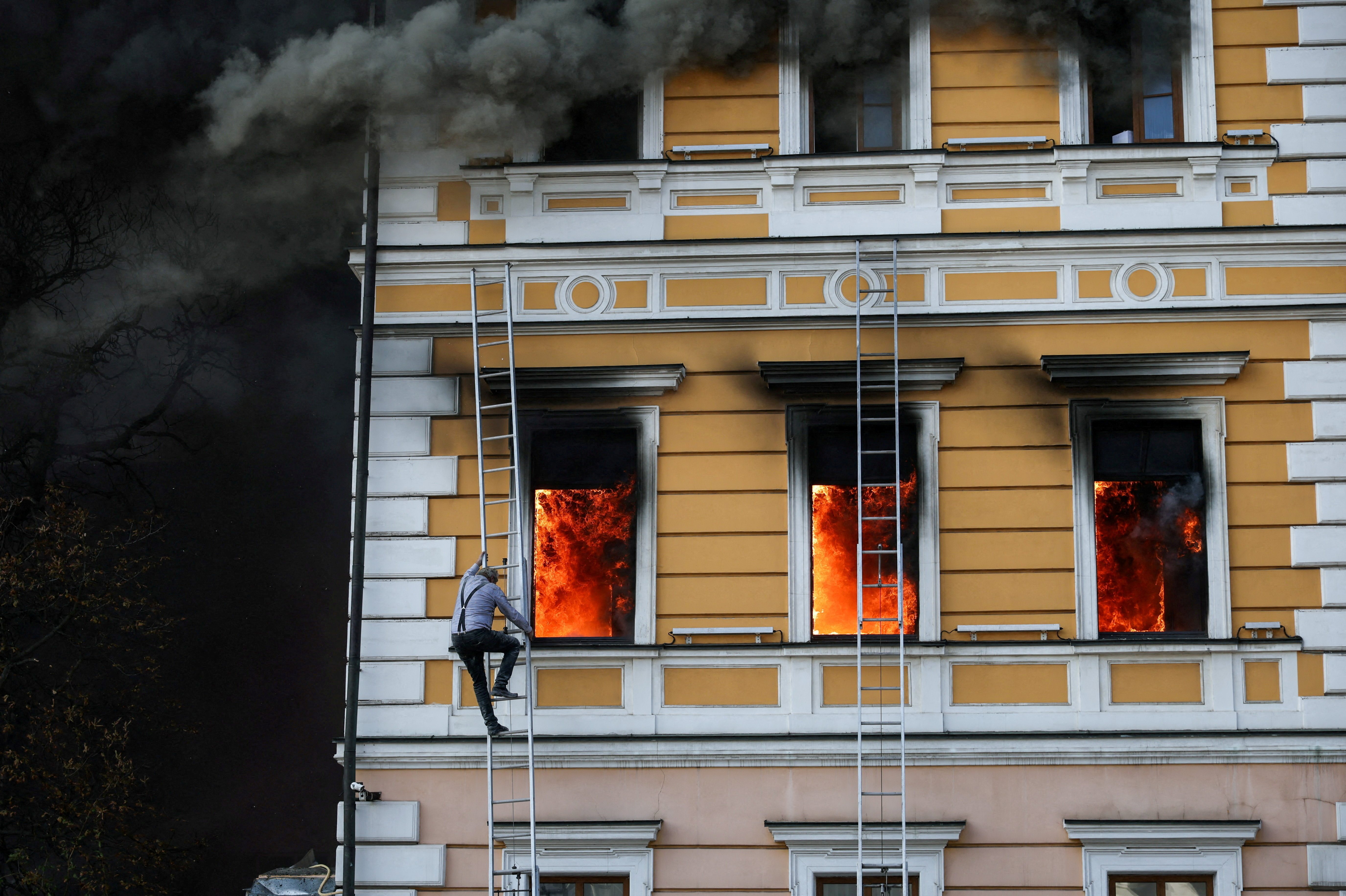 Ihor Malchevsky, 69, a deputy department head at Ukraine’s National Academy of Sciences, uses a ladder as flames rise from an administrative building hit by a Russian jet-powered drone attack, in Kyiv, Ukraine, September 28, 2026