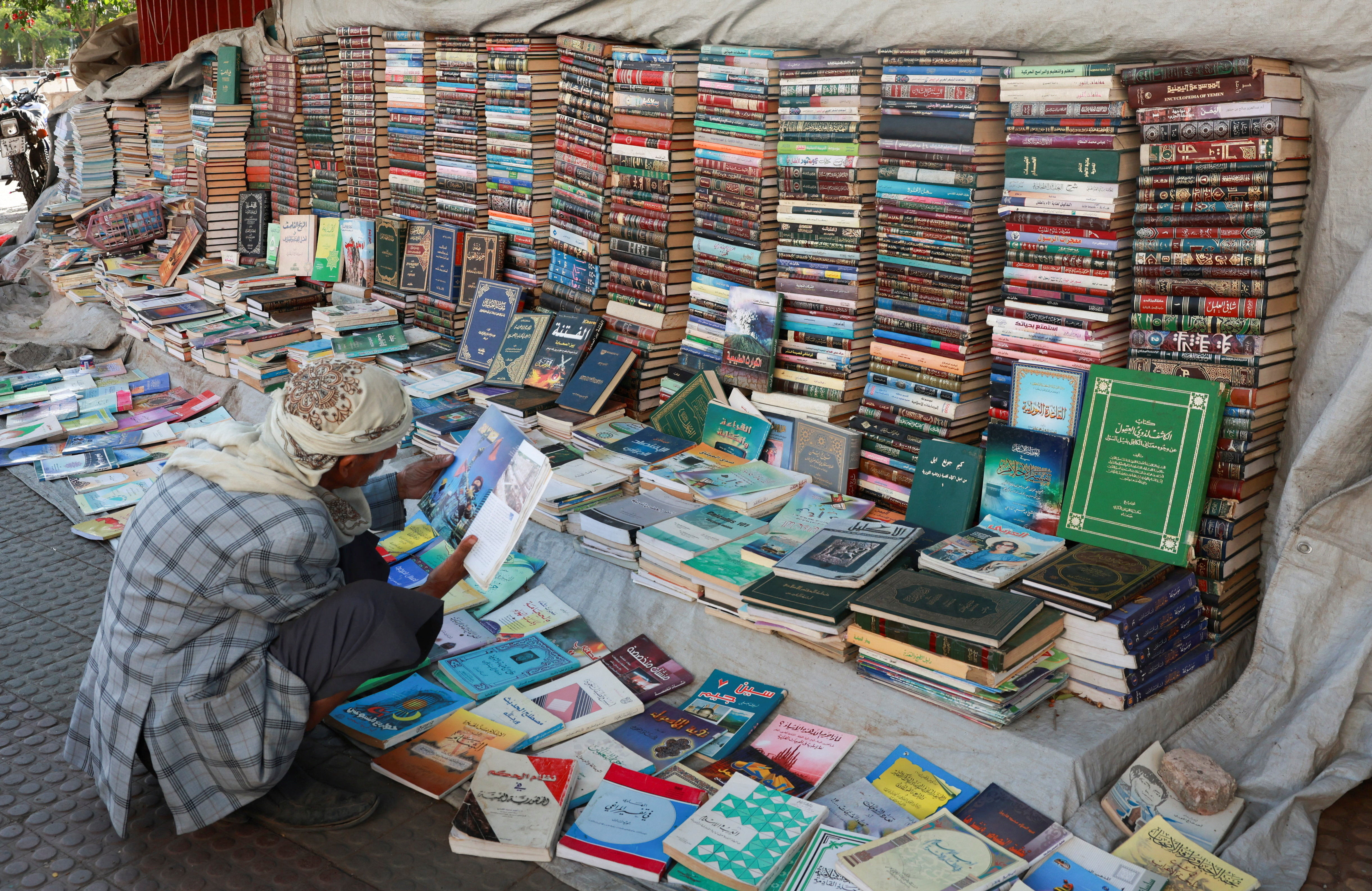 A man reads a book as he browses used books displayed for sale on a street in Sanaa, Yemen, October 8, 2026. [Mohammed al-Mahdi / REUTERS]